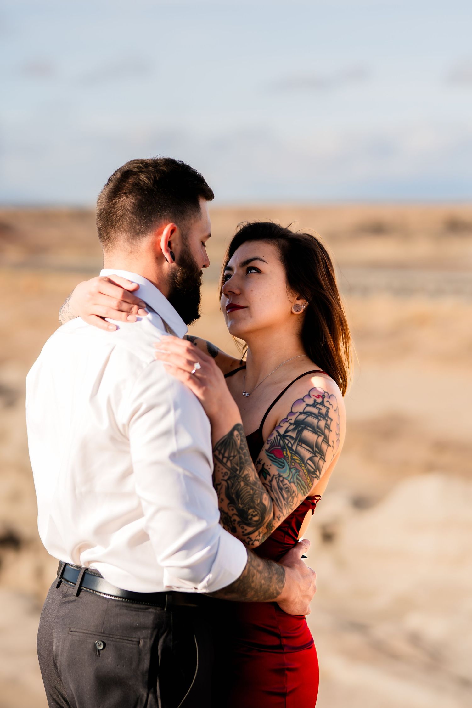A couple in formal attire embracing in a desert landscape during golden hour.