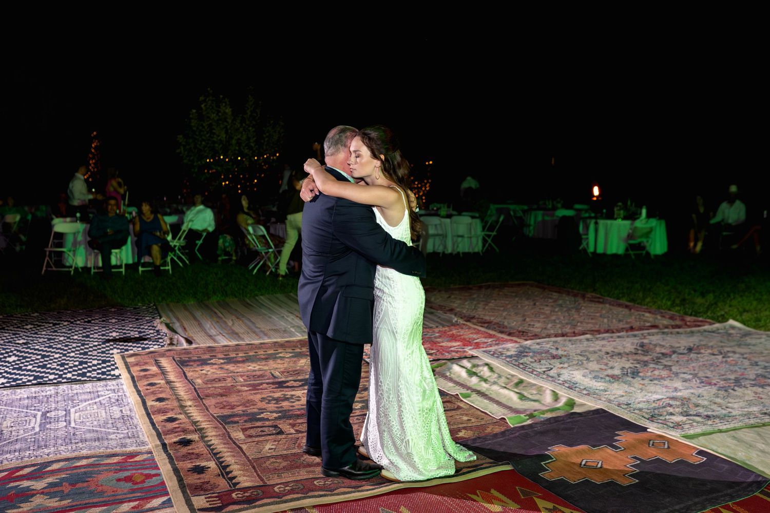 Couple dances on ornate rug under night sky at outdoor reception venue.