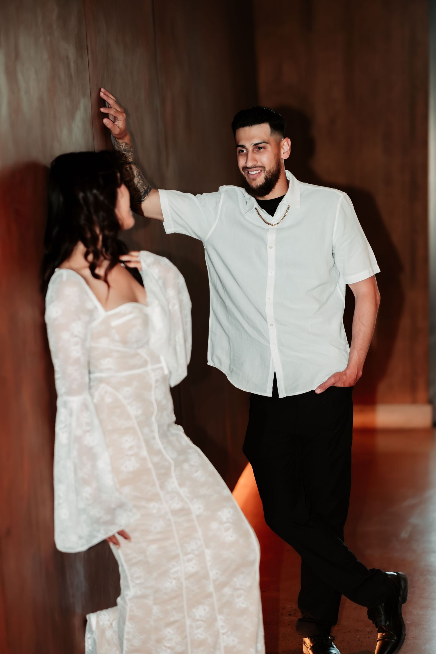 Couple in white and black attire sharing a joyful moment in a dimly lit hallway.
