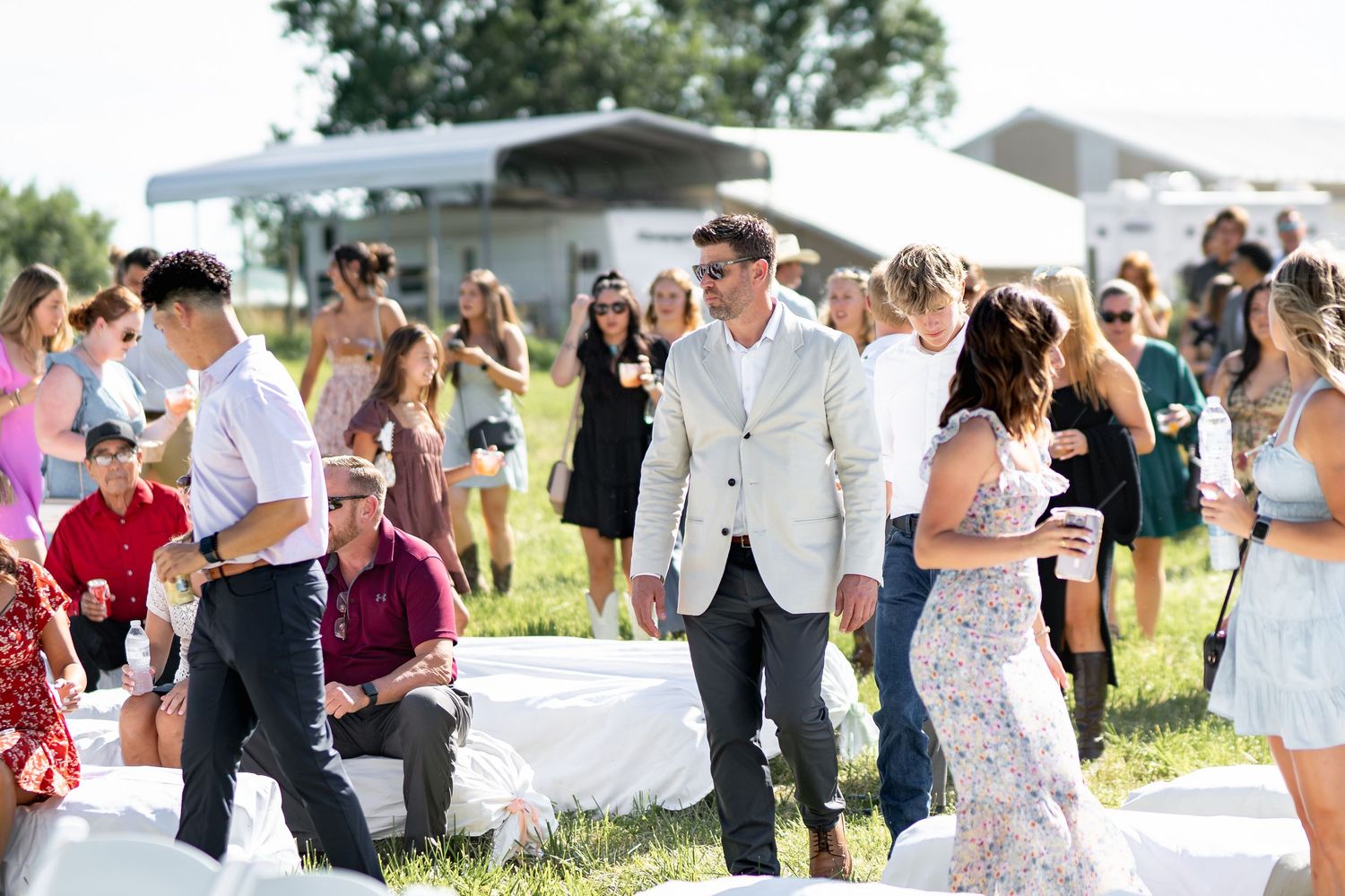 Guests gather outdoors at a summer wedding ceremony with white chairs and decorative elements.