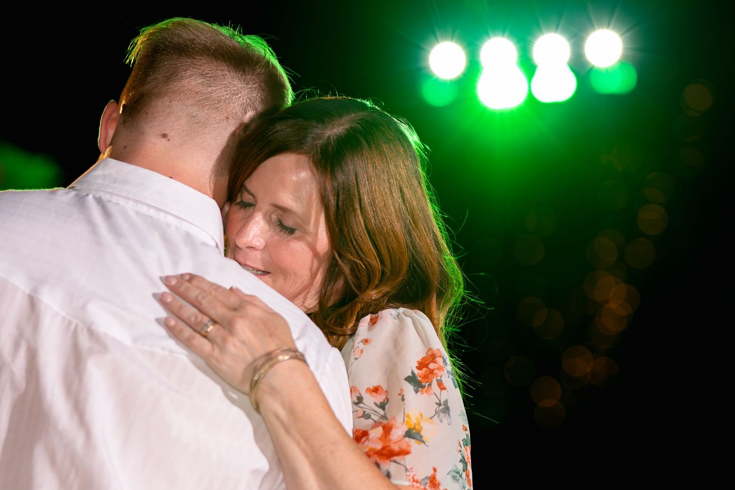 An emotional dance moment captured under green stage lighting at an evening wedding reception.