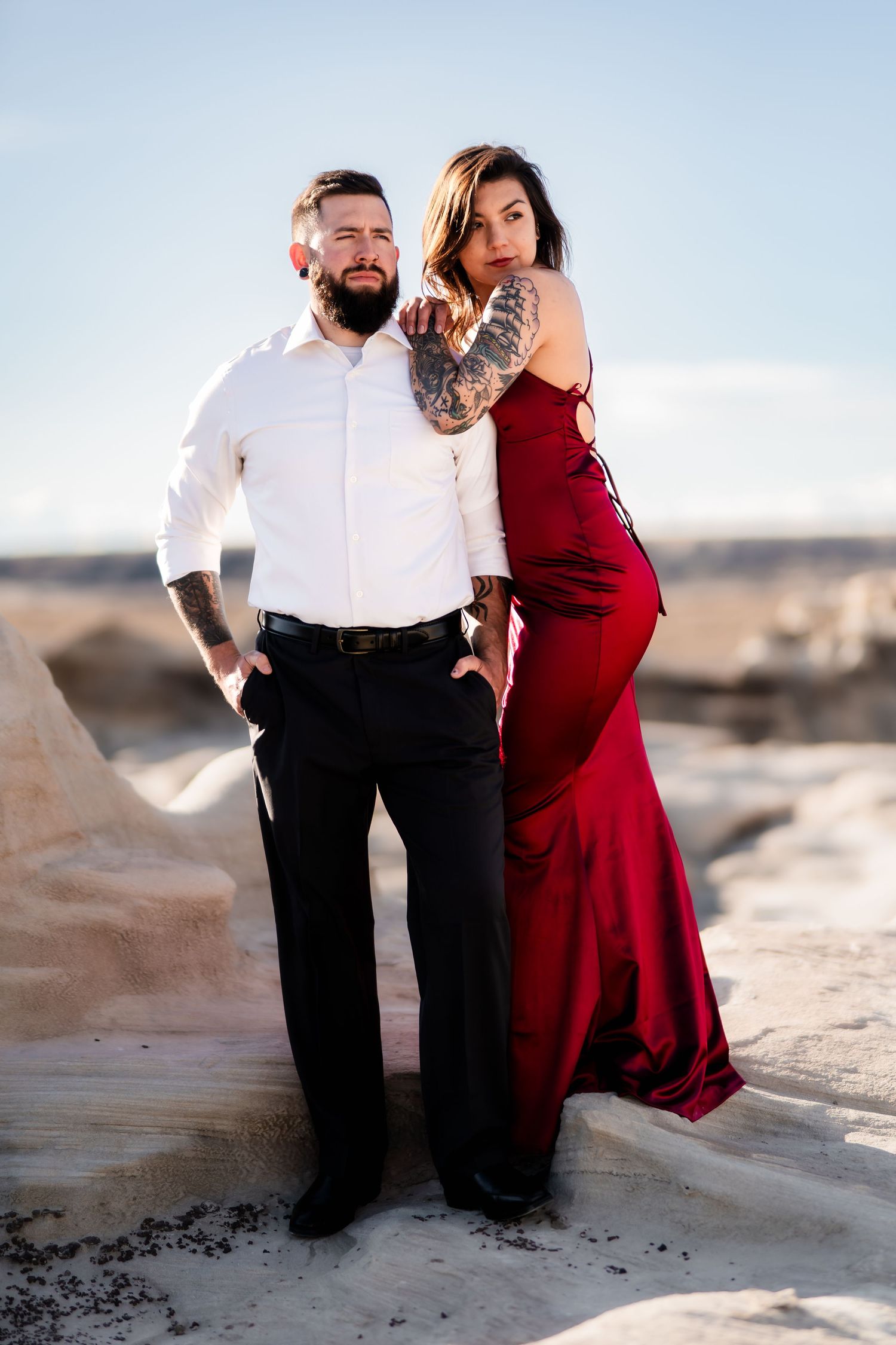Stylish couple in formal attire posing on rocky terrain during golden hour.
