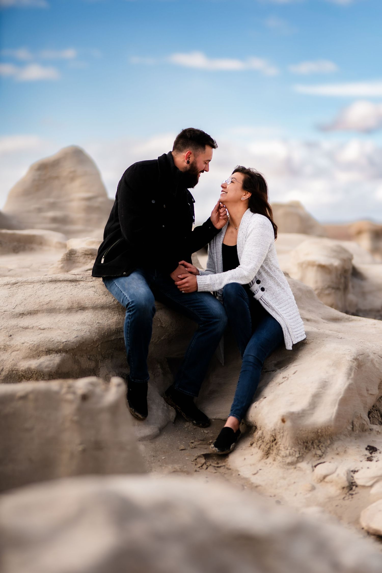 A couple laughs together while sitting on desert rocks on a sunny day.