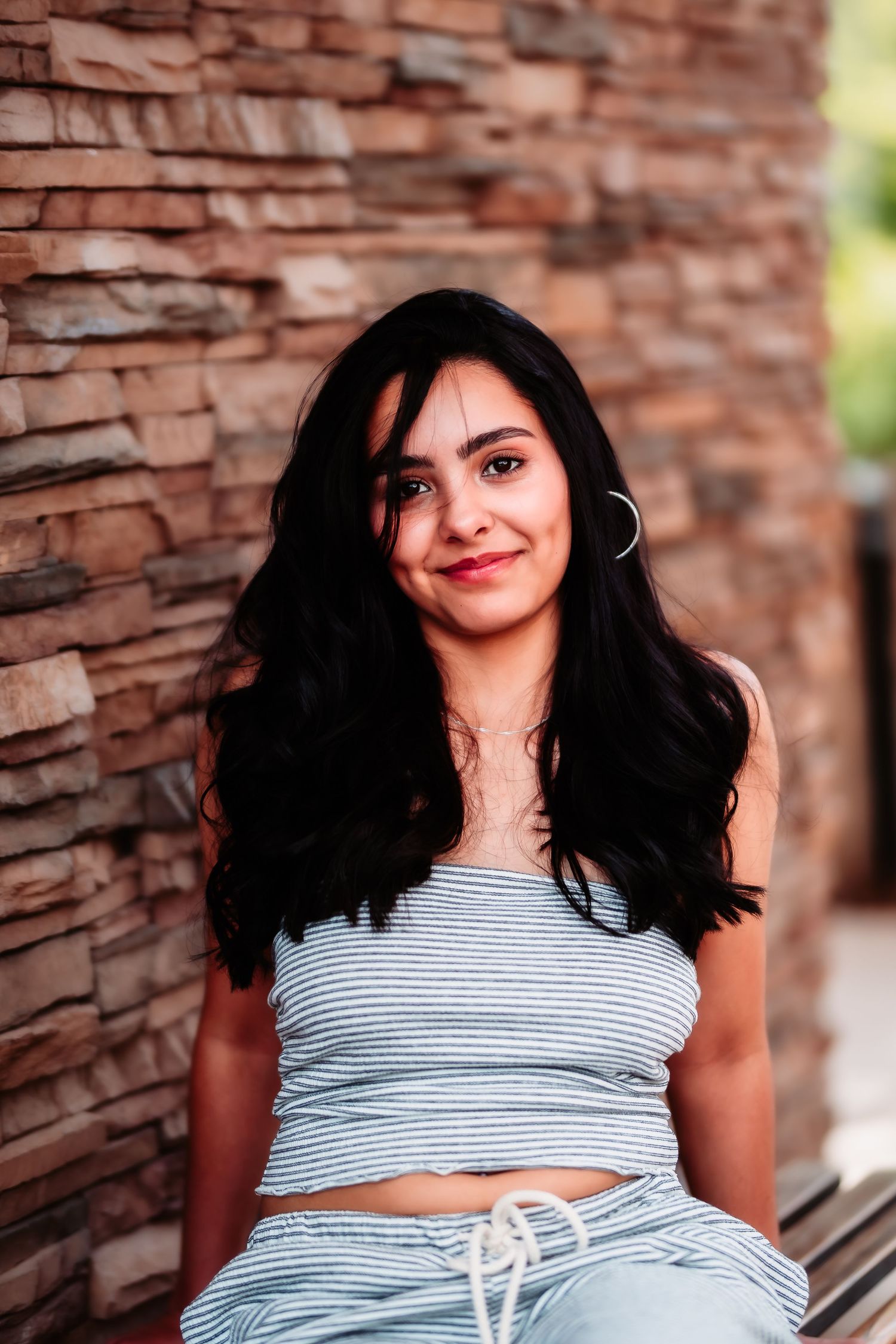 A casual summer portrait against a textured stone wall wearing a striped outfit.