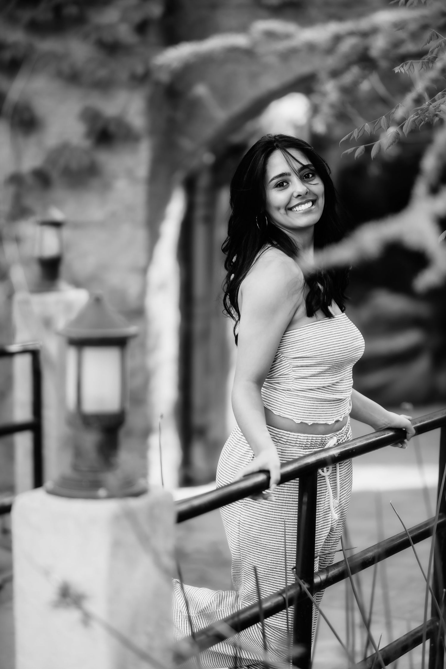 Black and white portrait of woman smiling while leaning on railing with architectural details behind.