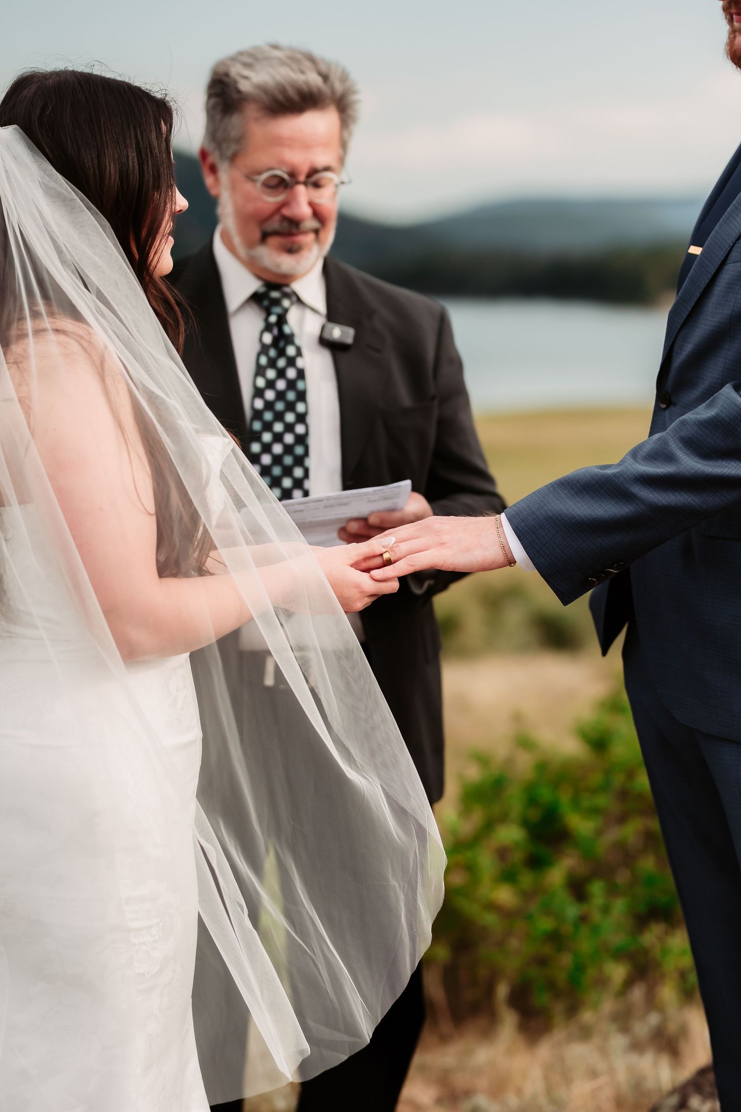 A wedding ceremony taking place outdoors with the exchange of rings in front of a scenic mountain backdrop.