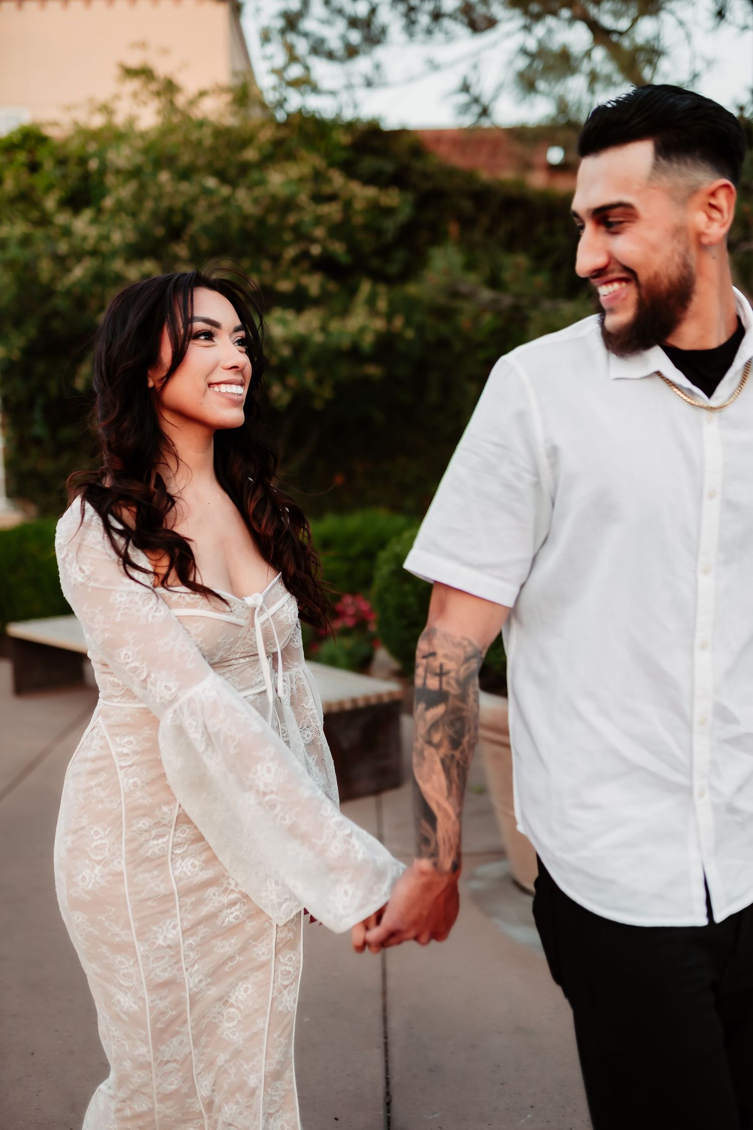 Couple in coordinated white outfits walking together outdoors during golden hour.