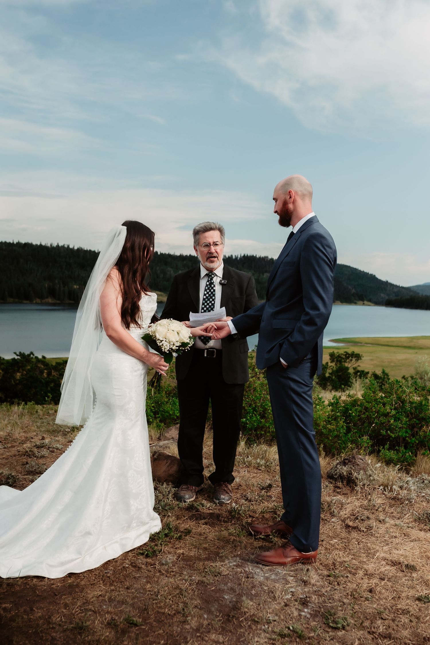 Wedding ceremony exchange of rings during outdoor mountain celebration.