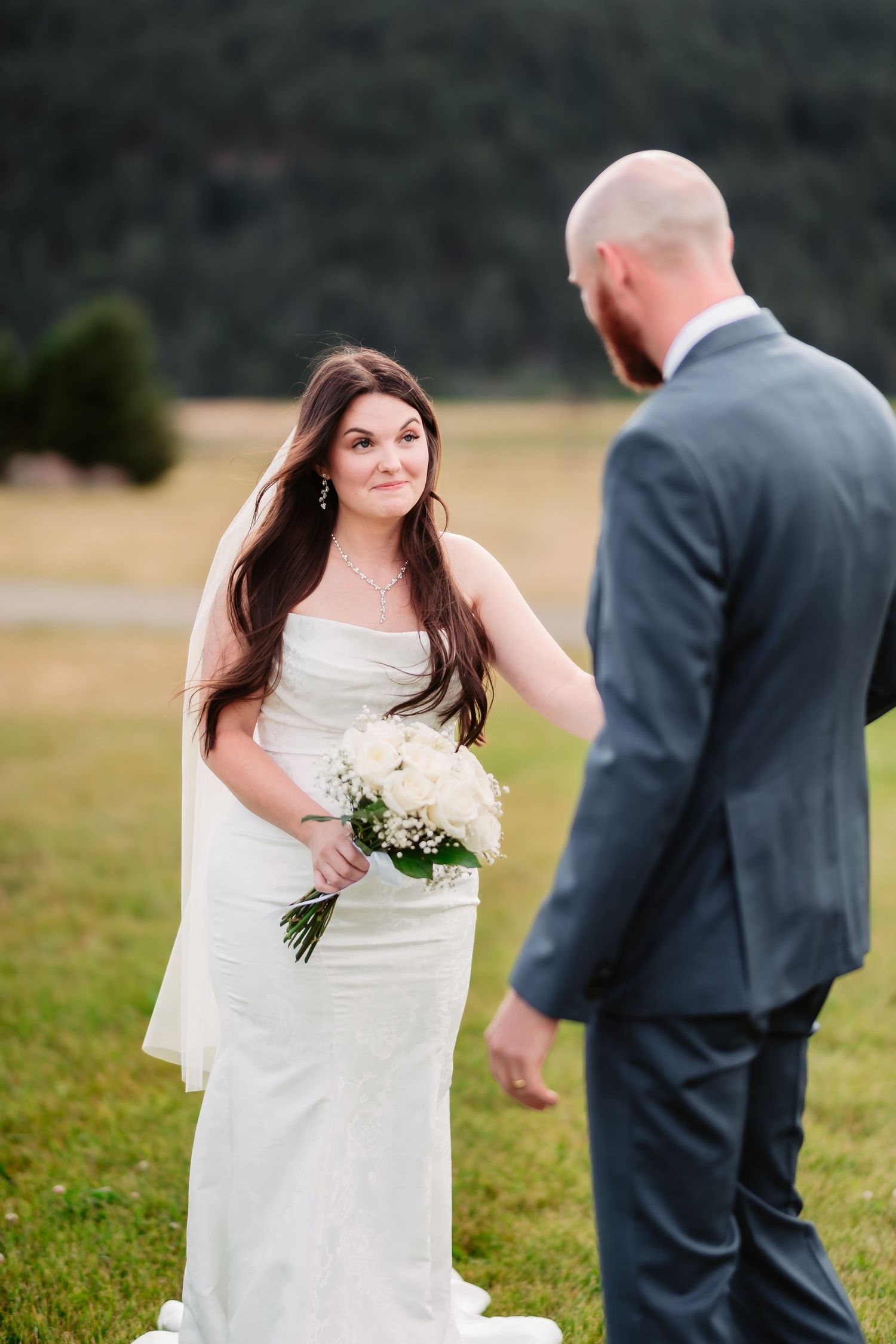 A bride in a white gown and groom in dark suit having their first look moment outdoors.