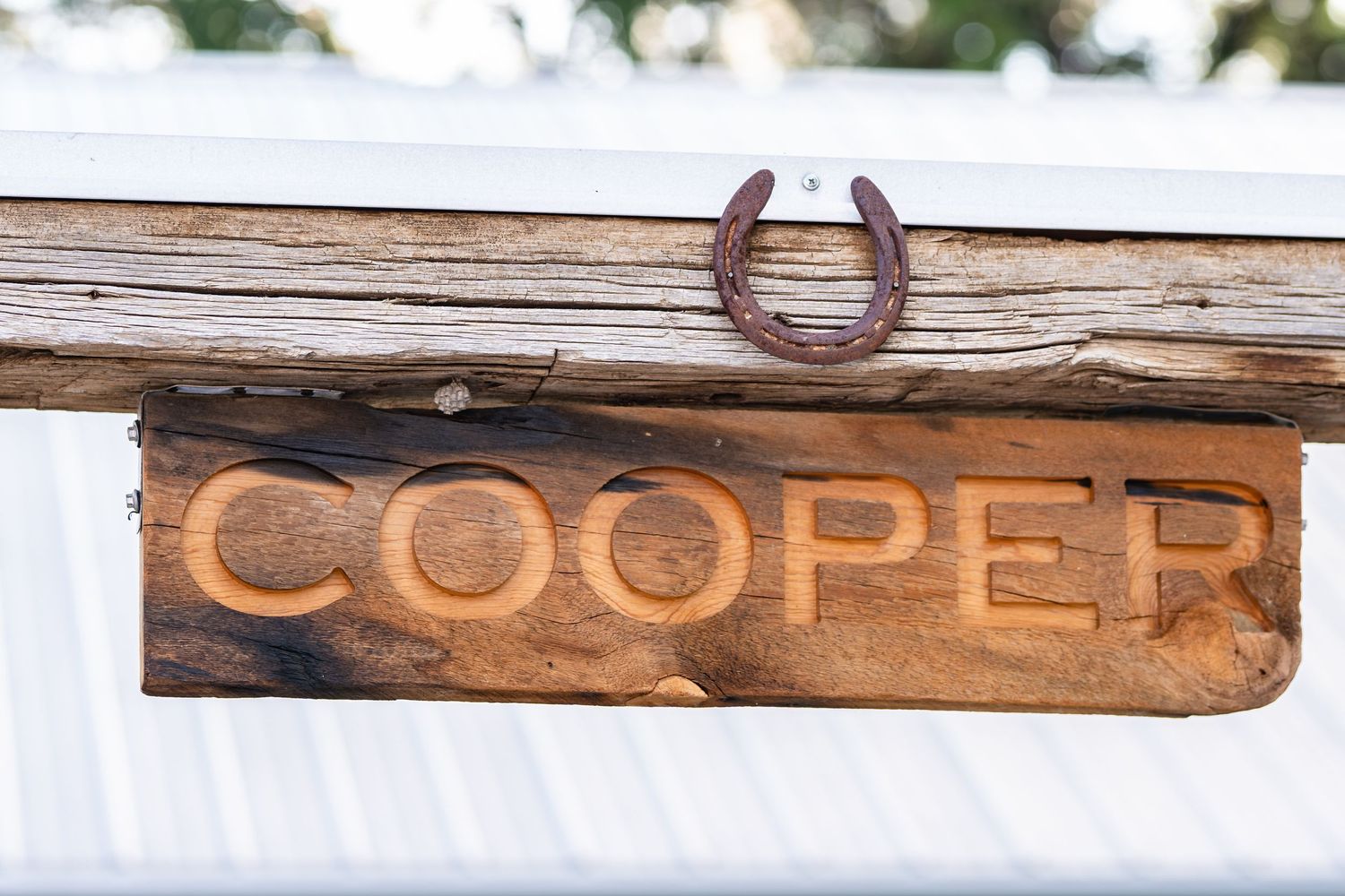 A wooden sign reading 'Cooper' with a horseshoe mounted above it on weathered wood.