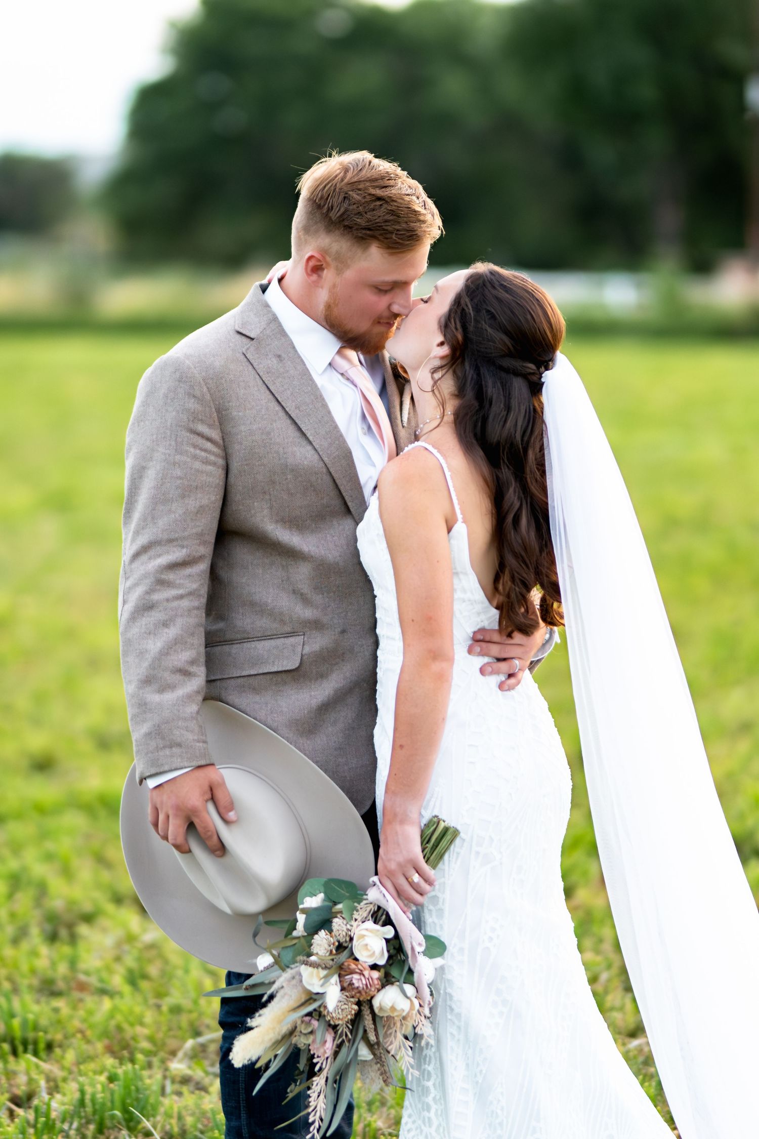 Romantic wedding portrait in green field with elegant attire and flowing veil.