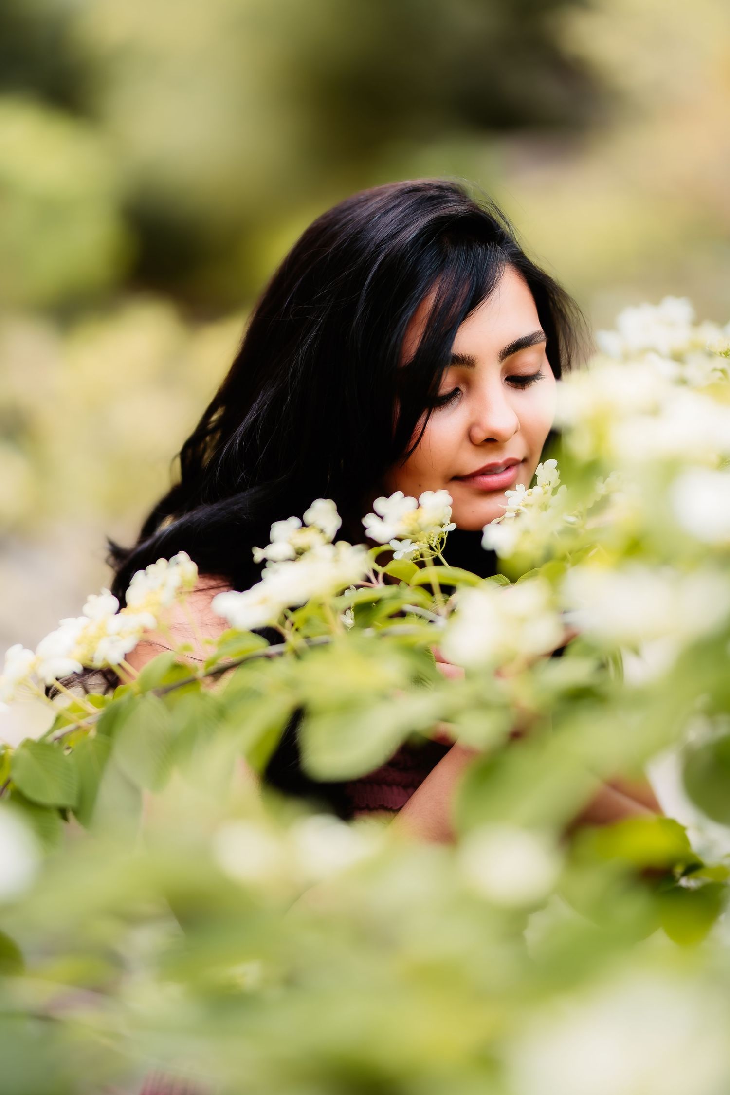 Close-up portrait among white flowers and green leaves in soft natural lighting.