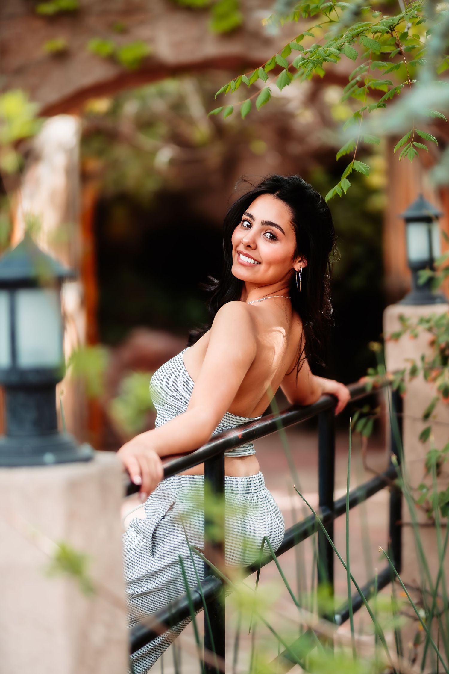 A candid portrait on a balcony with striped attire and natural foliage in the background.