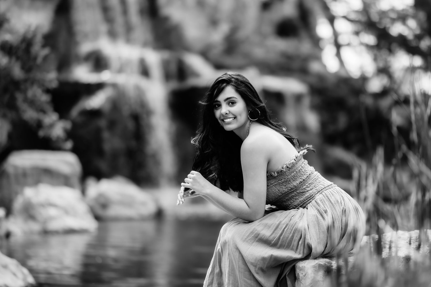 Black and white photo of someone in an elegant dress posing near a waterfall.