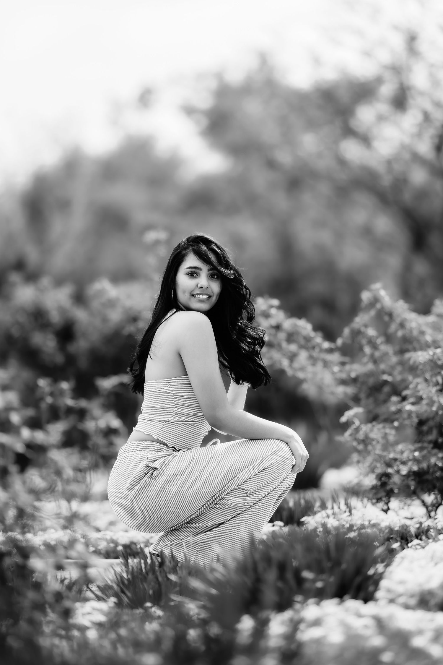 Black and white photo of woman in casual attire kneeling among garden flowers.