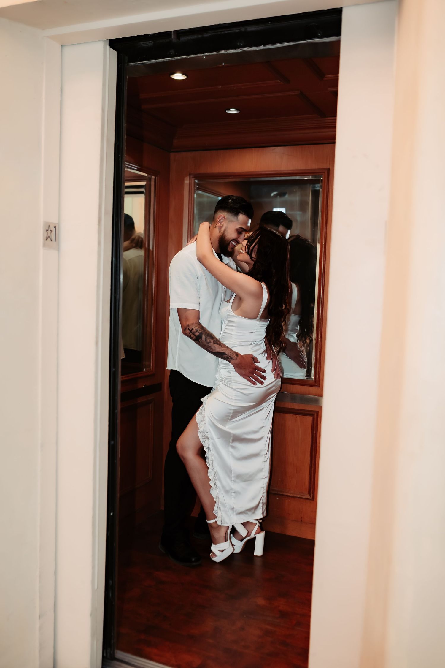 Romantic doorway scene of couple in white formal wear embracing in warm interior lighting.