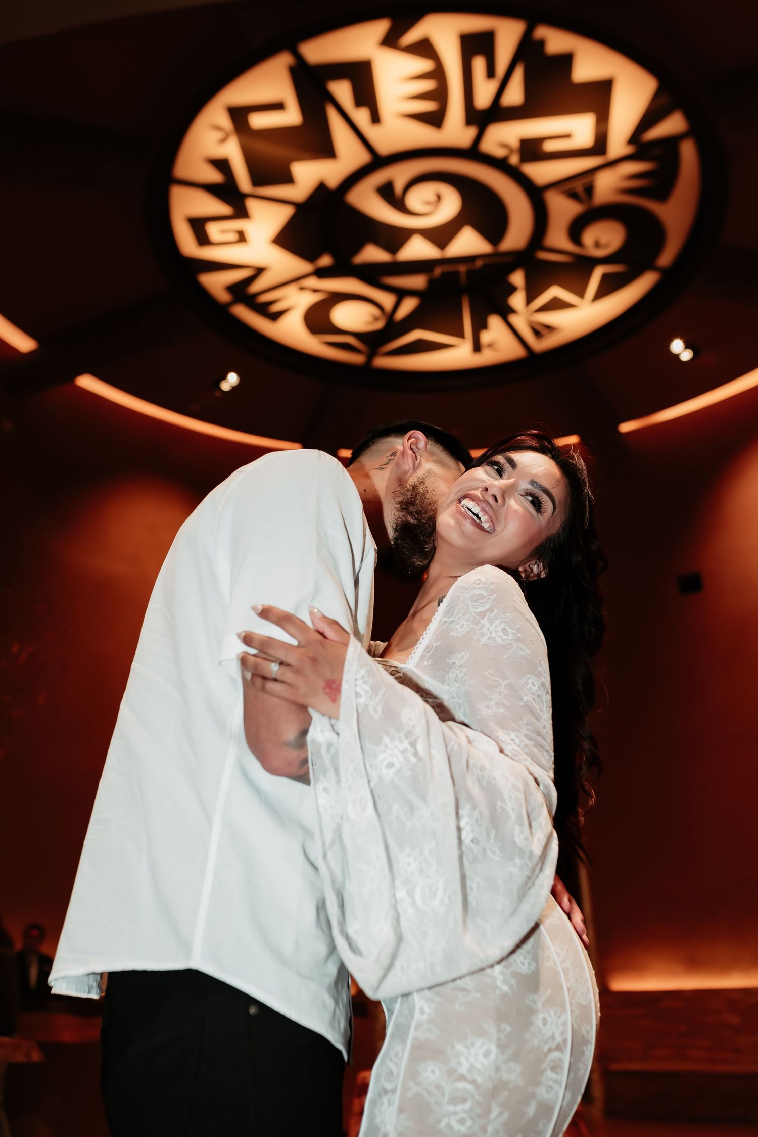 Couple dancing and laughing under decorative ceiling art in warm lighting.