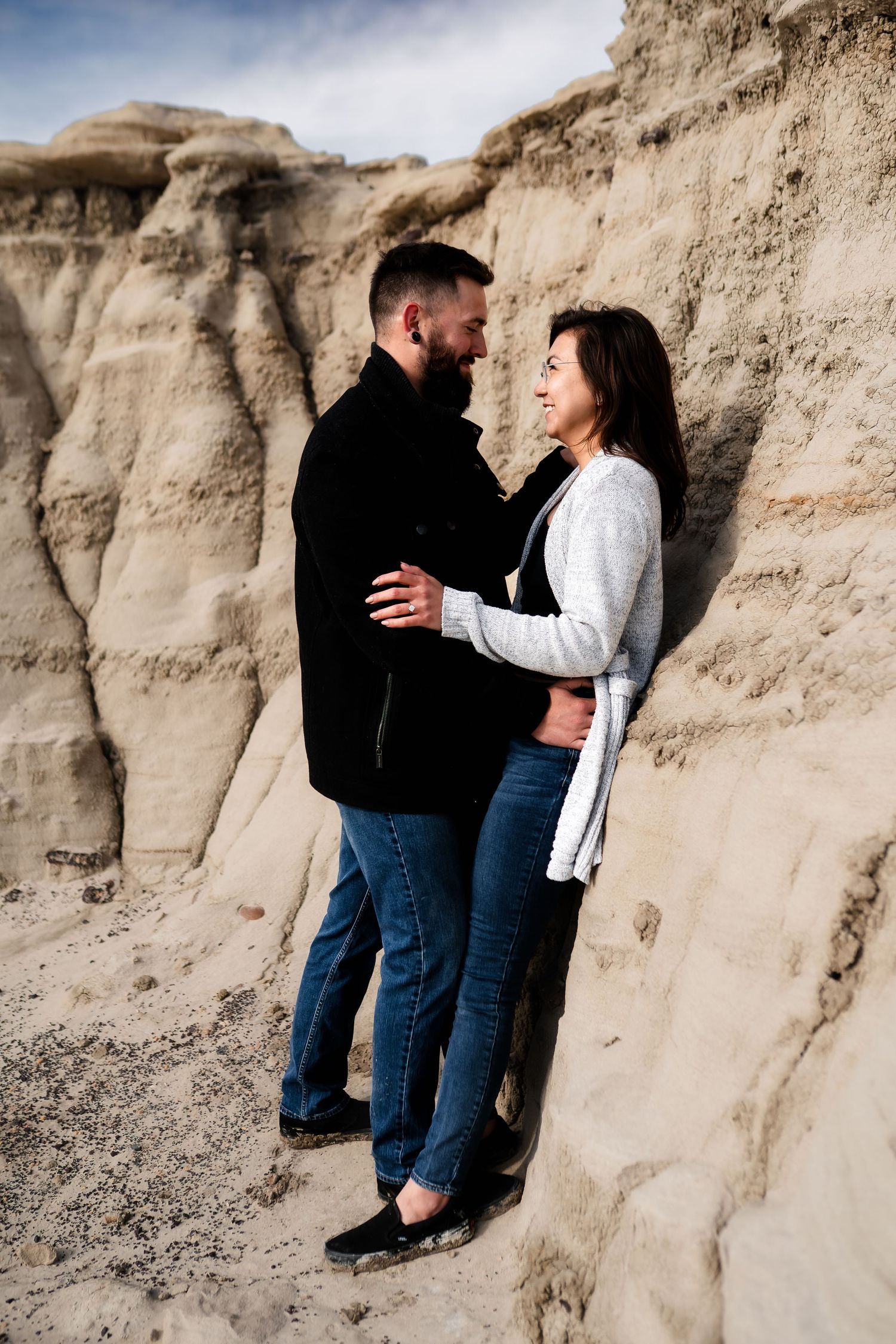 A couple embraces while standing against textured rock formations in a desert landscape.