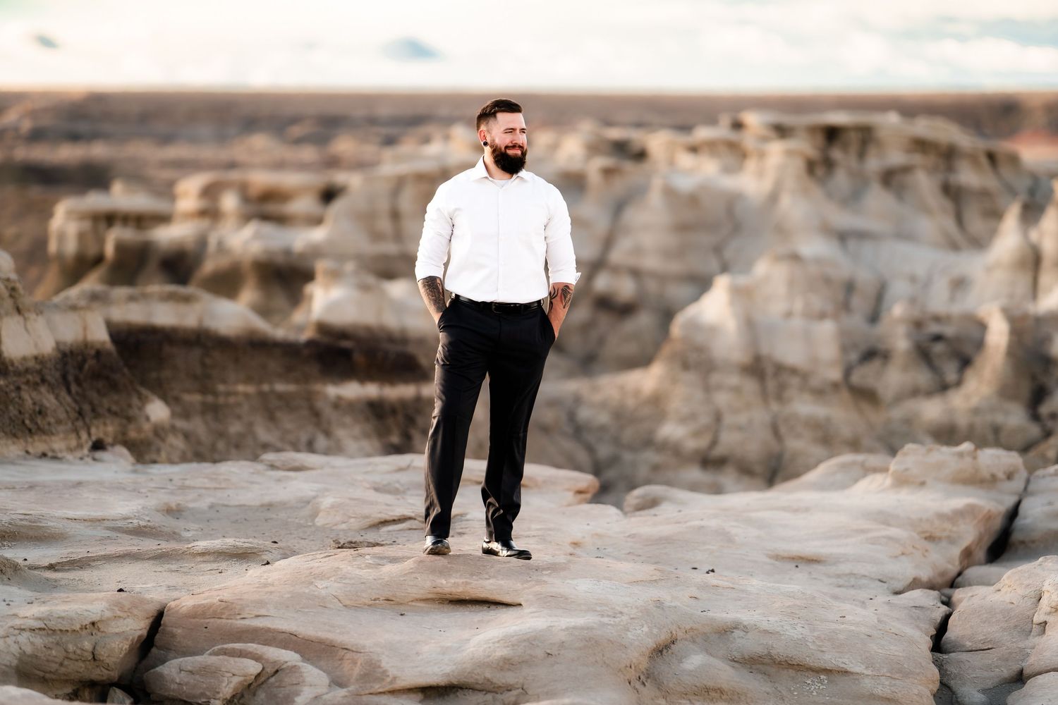A person in formal white attire poses confidently on textured desert rocks.