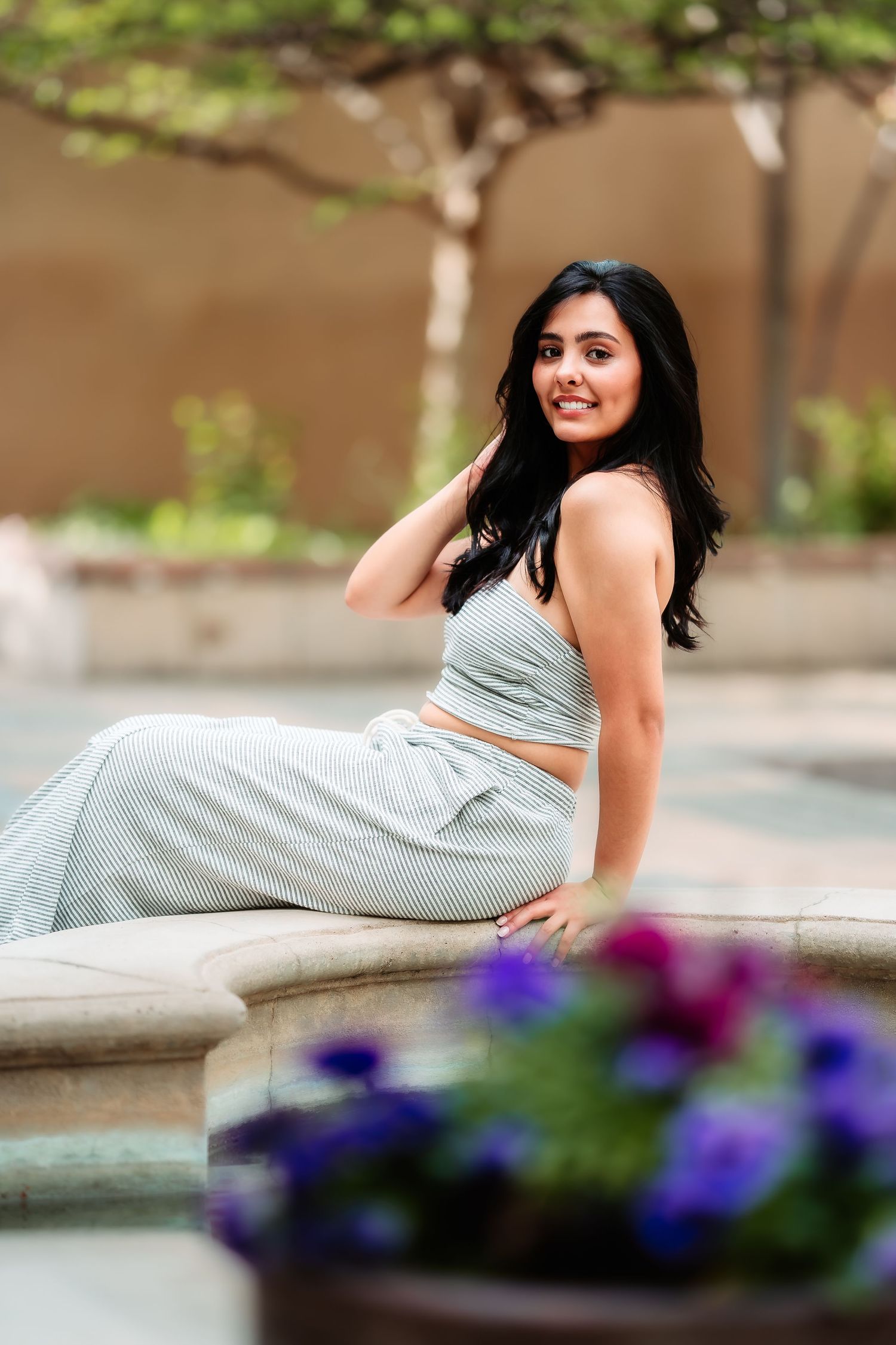A casual lifestyle portrait by a fountain with purple flowers in foreground.