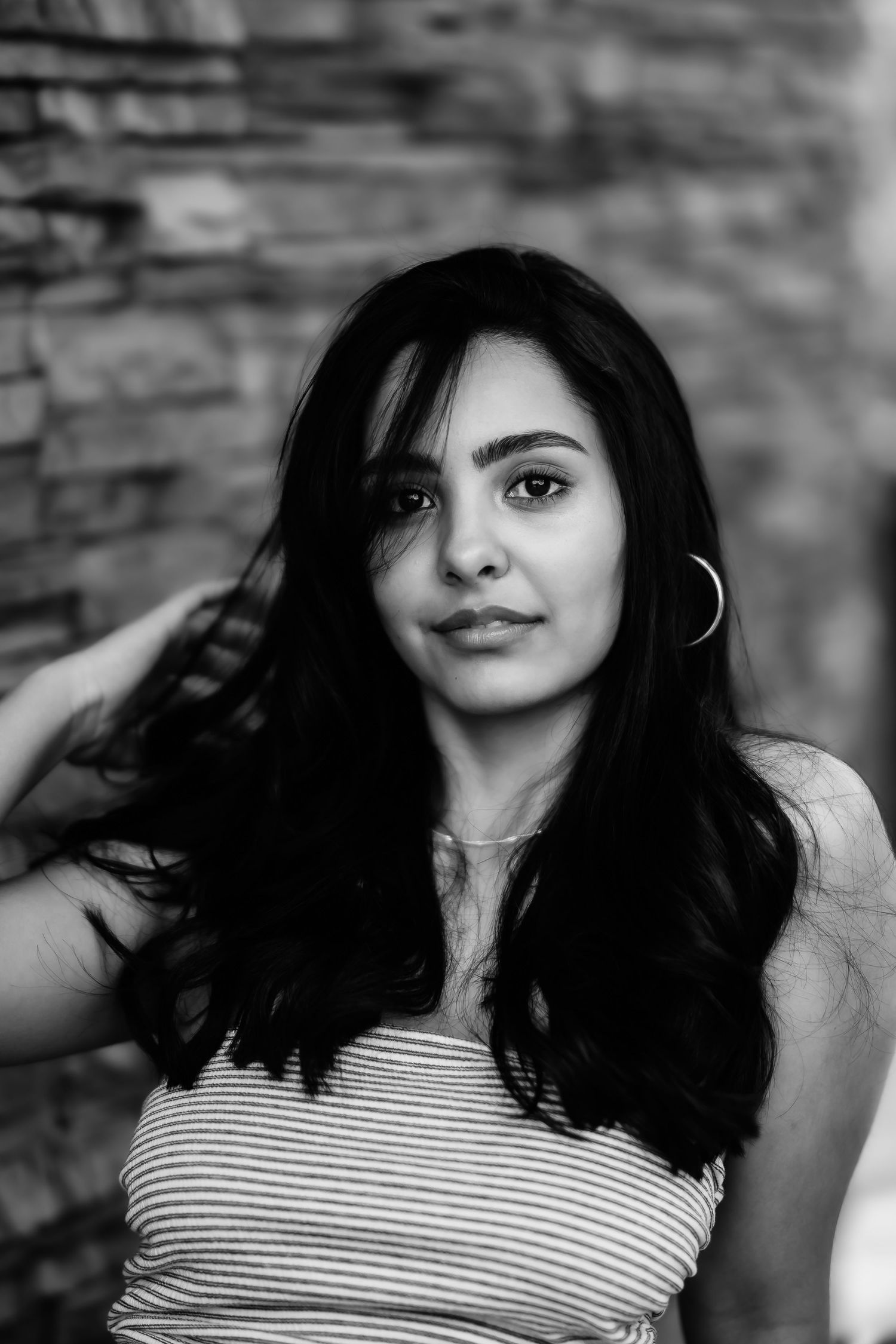 A close-up black and white portrait showing someone with long dark hair against a stone backdrop.