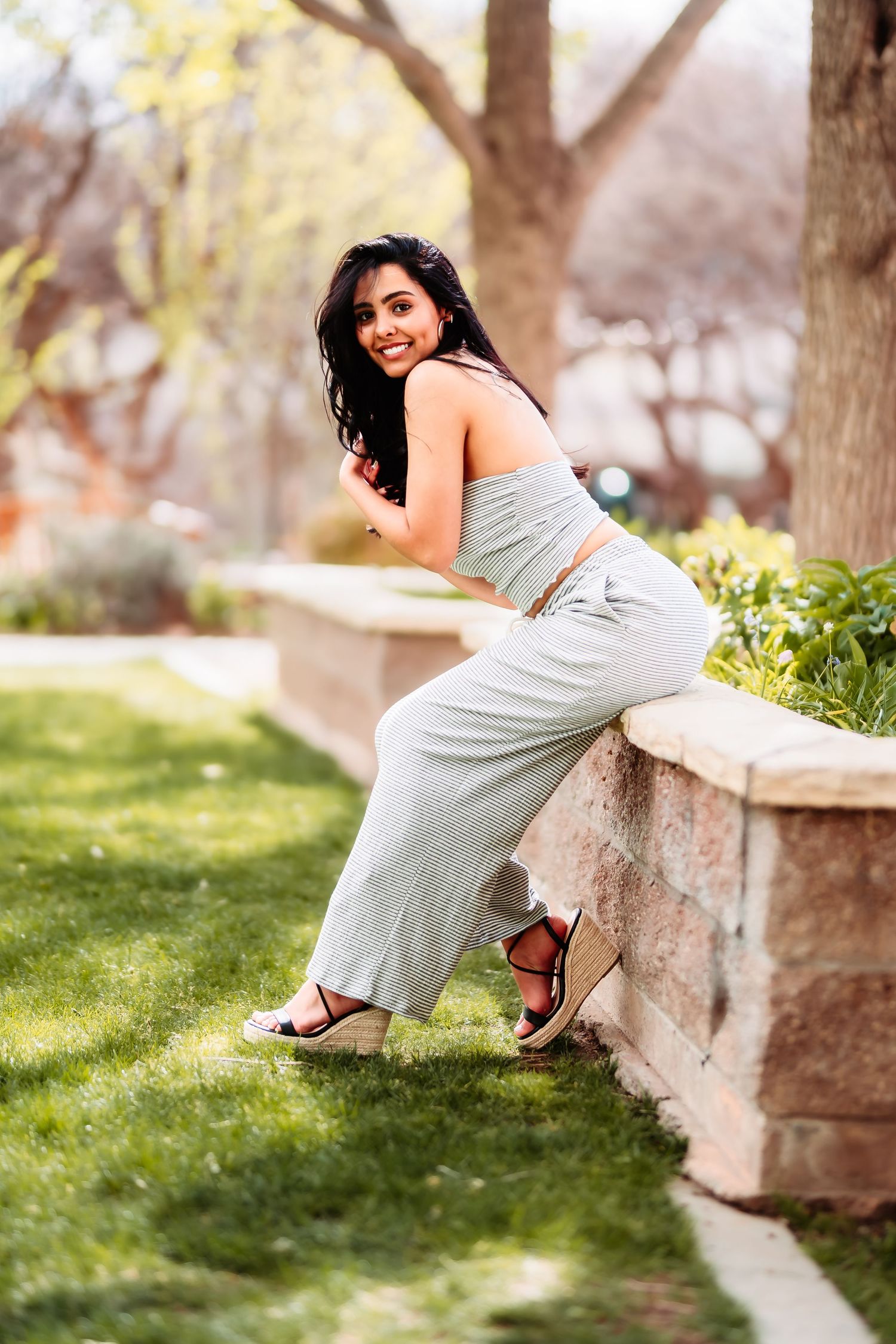 Candid shot of someone posing playfully against a stone wall in a sunny garden setting.