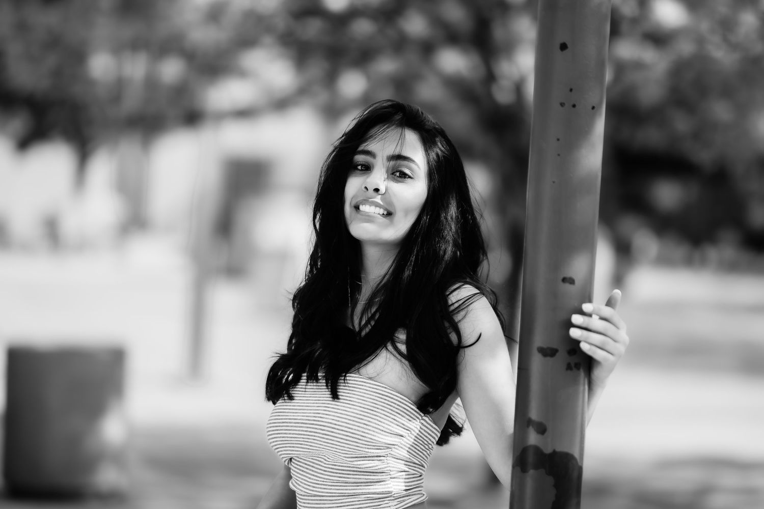 A candid black and white portrait showing someone in a striped top standing by a pole.