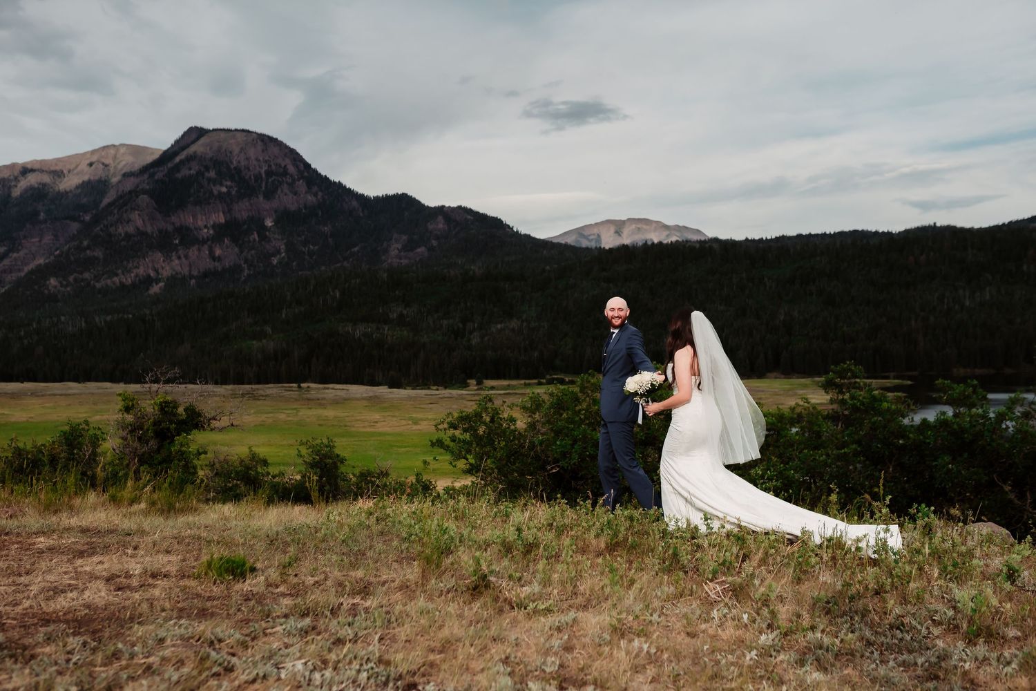 Wedding portrait on a mountainside with dramatic landscape and cloudy sky.