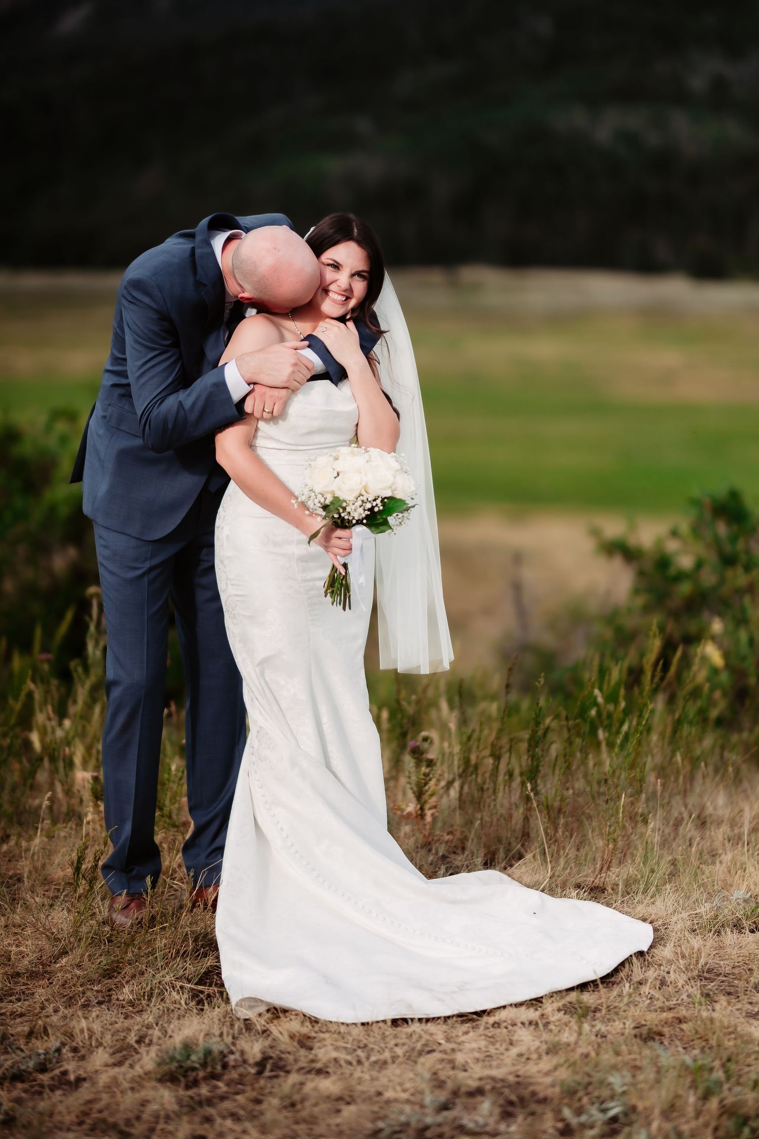 A sweet wedding moment captured in a field with mountains visible in the distance.