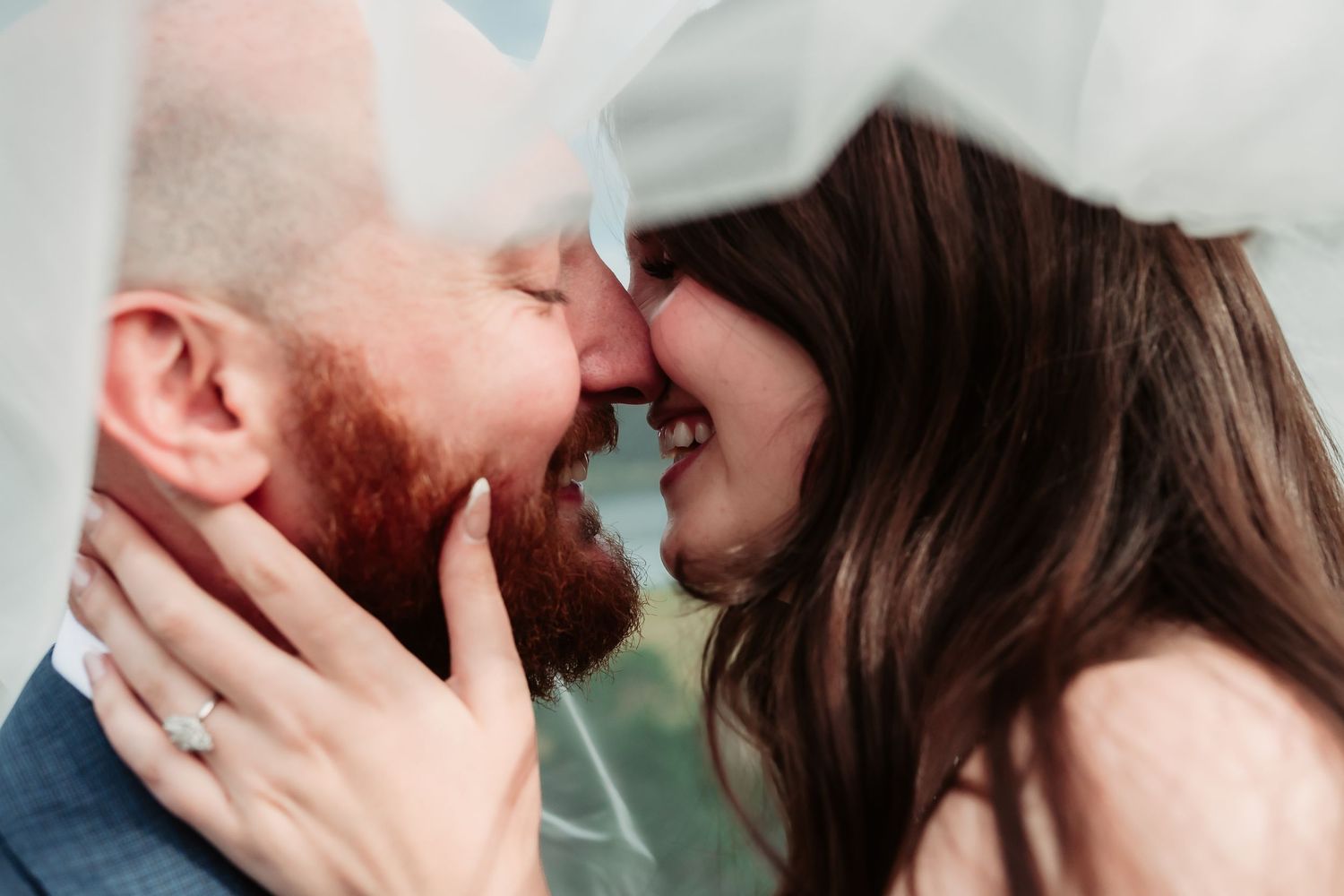 Close-up romantic moment under a delicate white veil against a soft background.