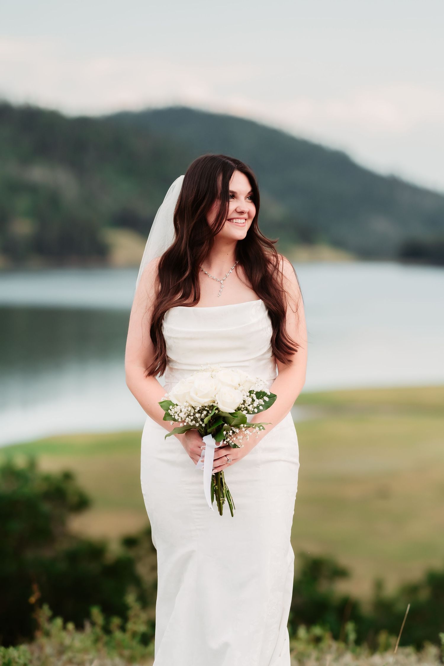 A bride in a white dress holds a bouquet against a mountainous landscape backdrop.