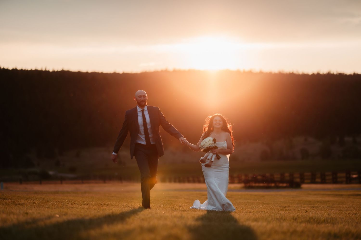 Wedding couple dances in golden sunset light across mountain meadow.