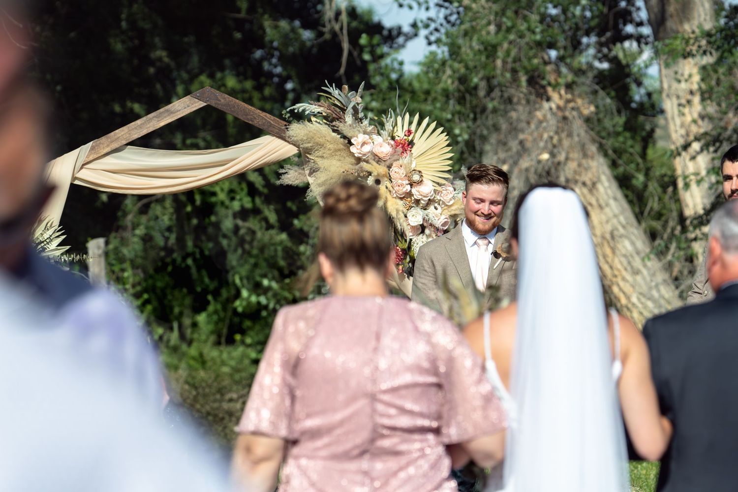Outdoor wedding ceremony setup with draped arch and dried flower arrangements in natural setting.