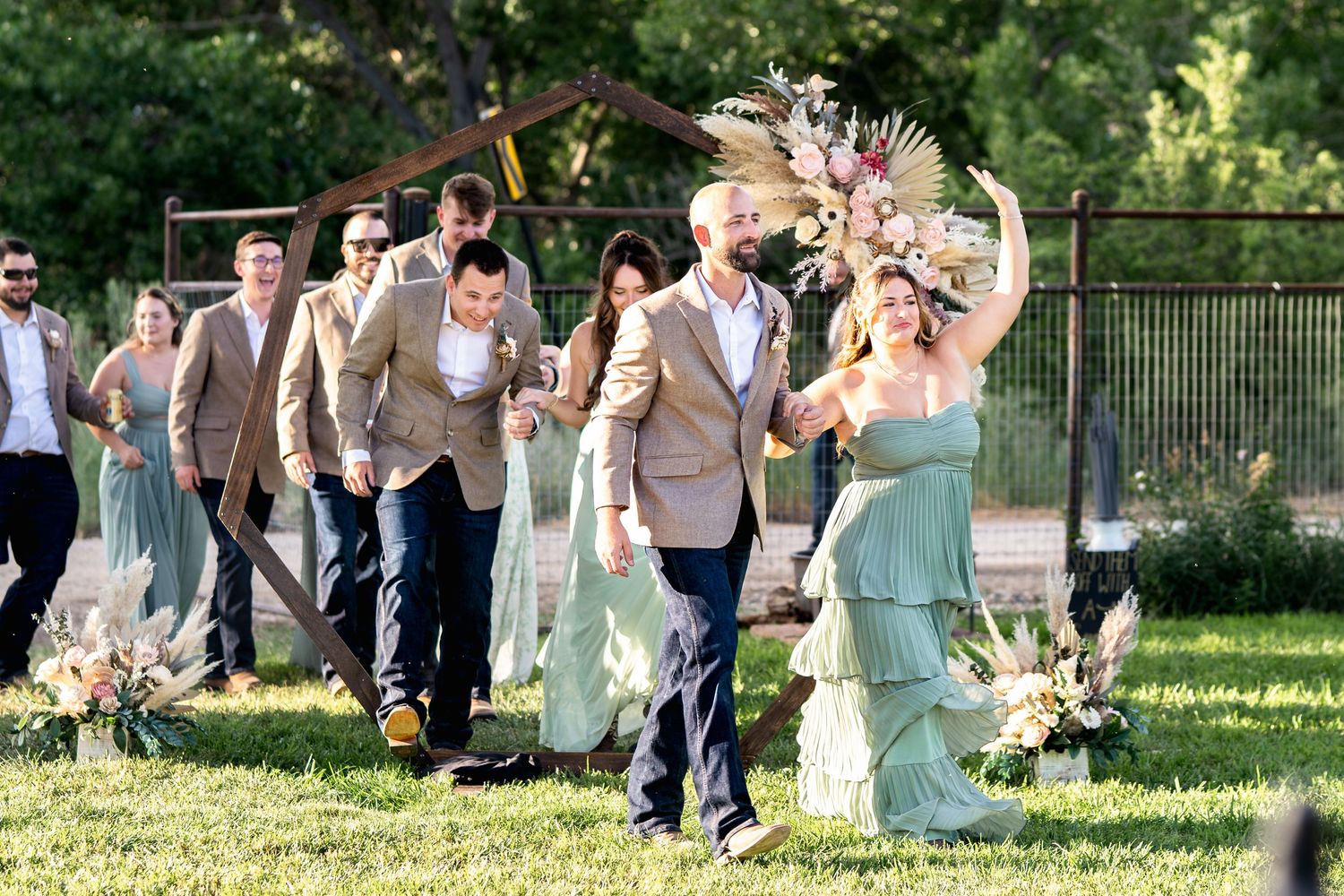 Wedding party joyfully walks on green lawn with bridesmaids in mint dresses and groomsmen in tan suits.