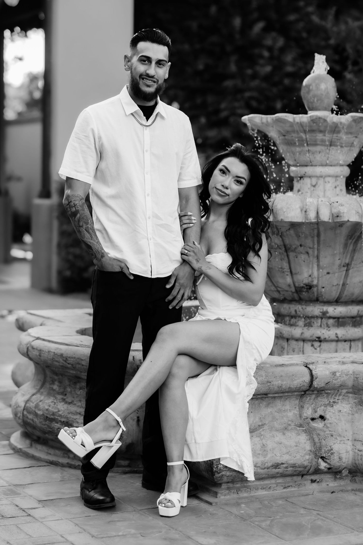 Black and white wedding photos show a couple posing near a stone fountain in elegant formal attire.
