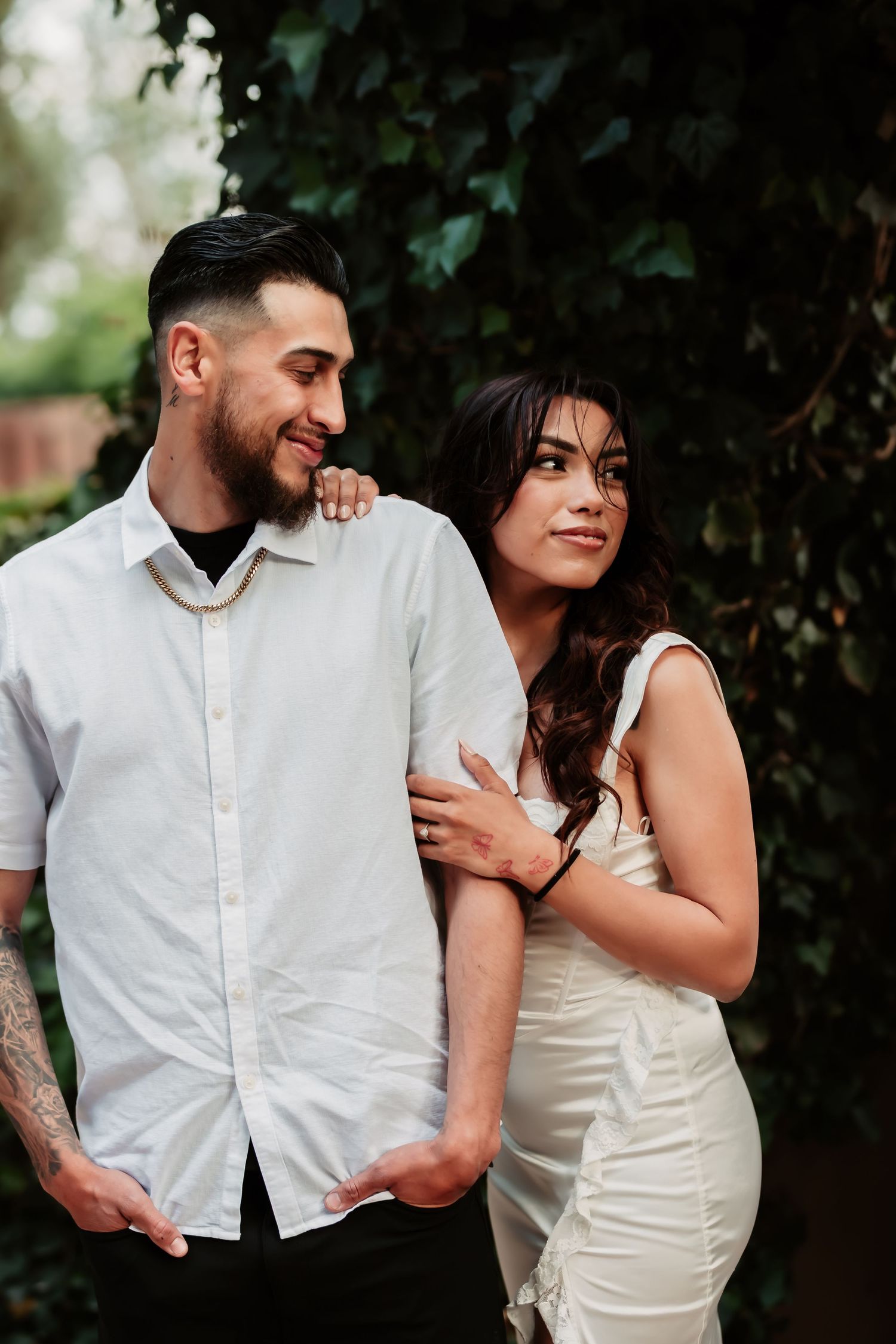 A romantic couple in white outfits share intimate moments against a lush green backdrop in a photo series.