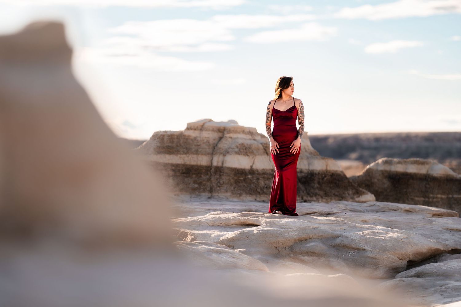 A figure in a flowing red dress stands gracefully on dramatic rock formations at sunset.