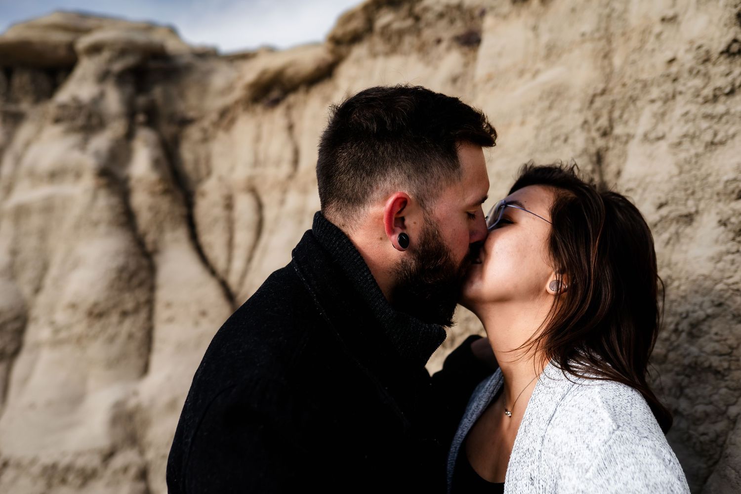A romantic couple shares a tender moment against rugged desert rock formations at sunset.