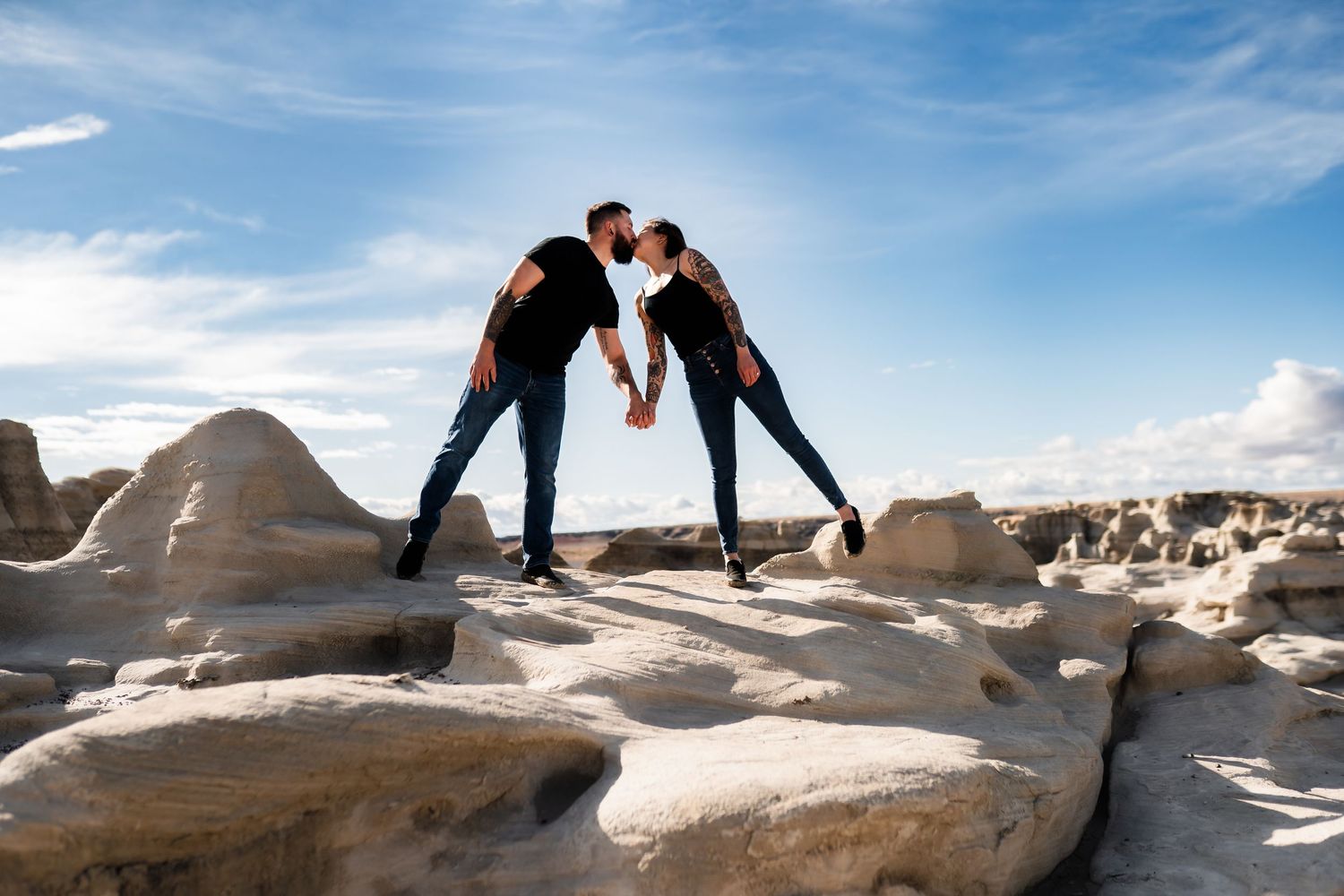 A couple poses together on white rock formations in a desert landscape under blue skies.