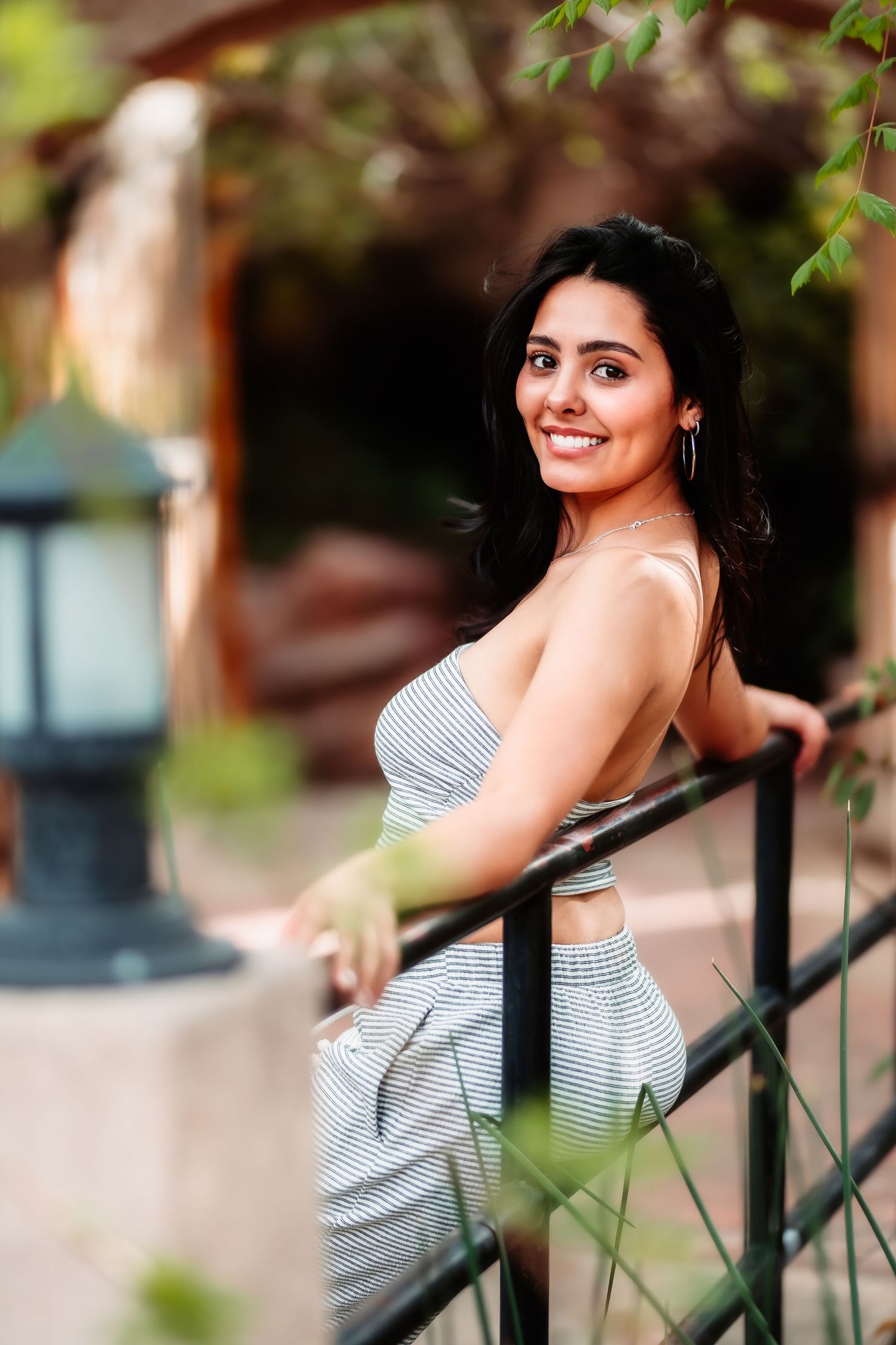 Natural light portrait by railing showcasing striped summer outfit and genuine smile.