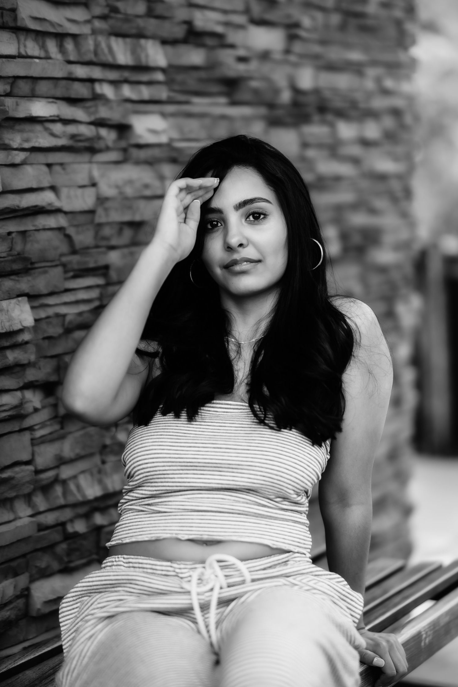 A black and white portrait of someone in striped clothing against a textured stone wall.