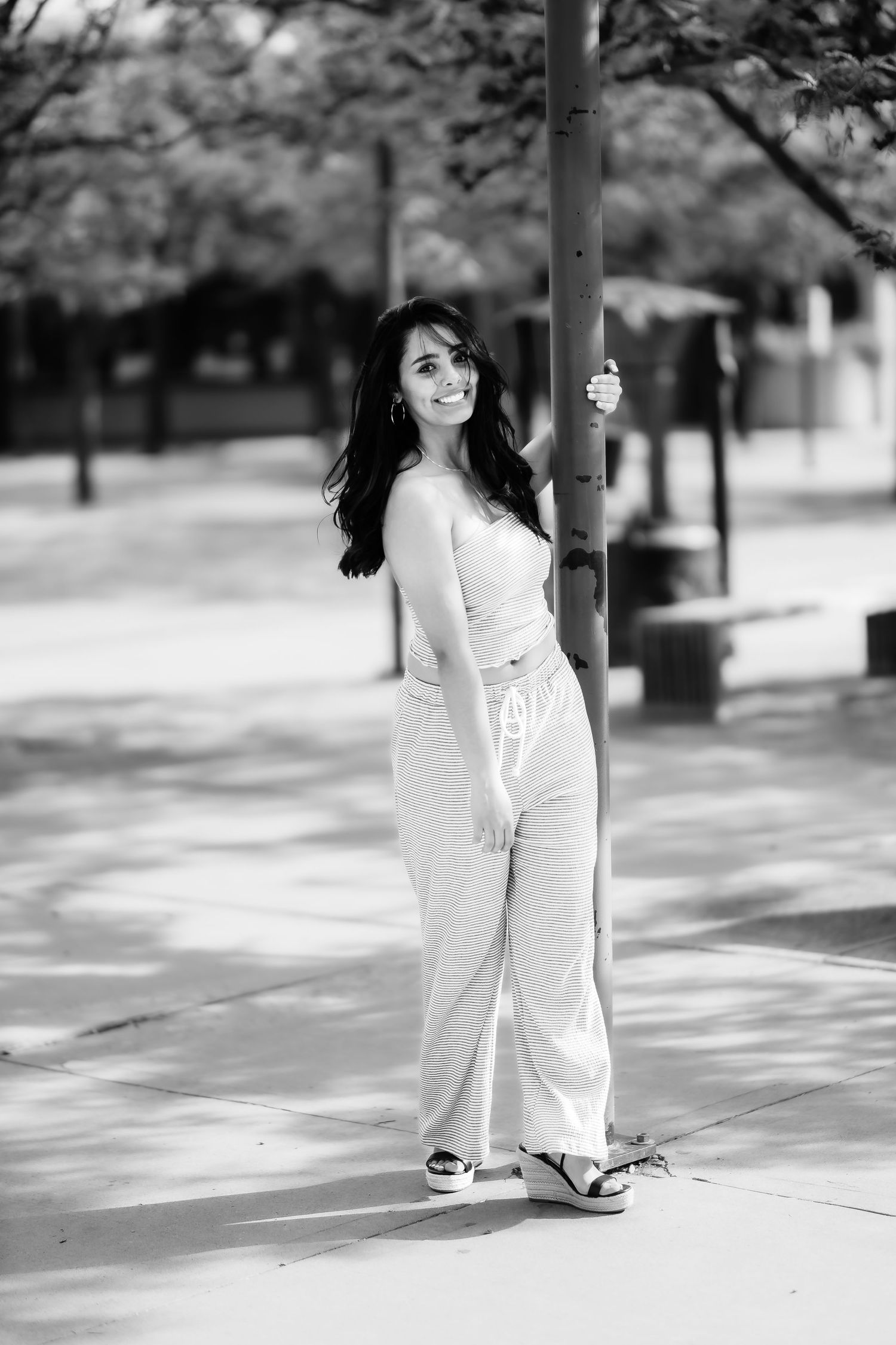 A full-length black and white portrait shows someone in casual wear posing beside a pole outdoors.