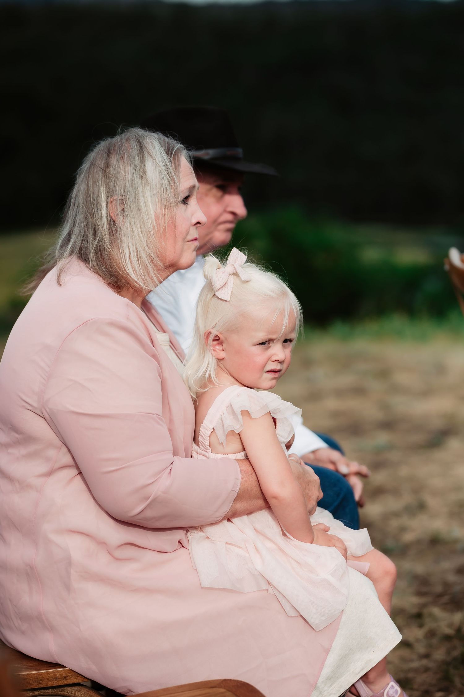 Family members in pink and white outfits sit together during an outdoor wedding celebration.