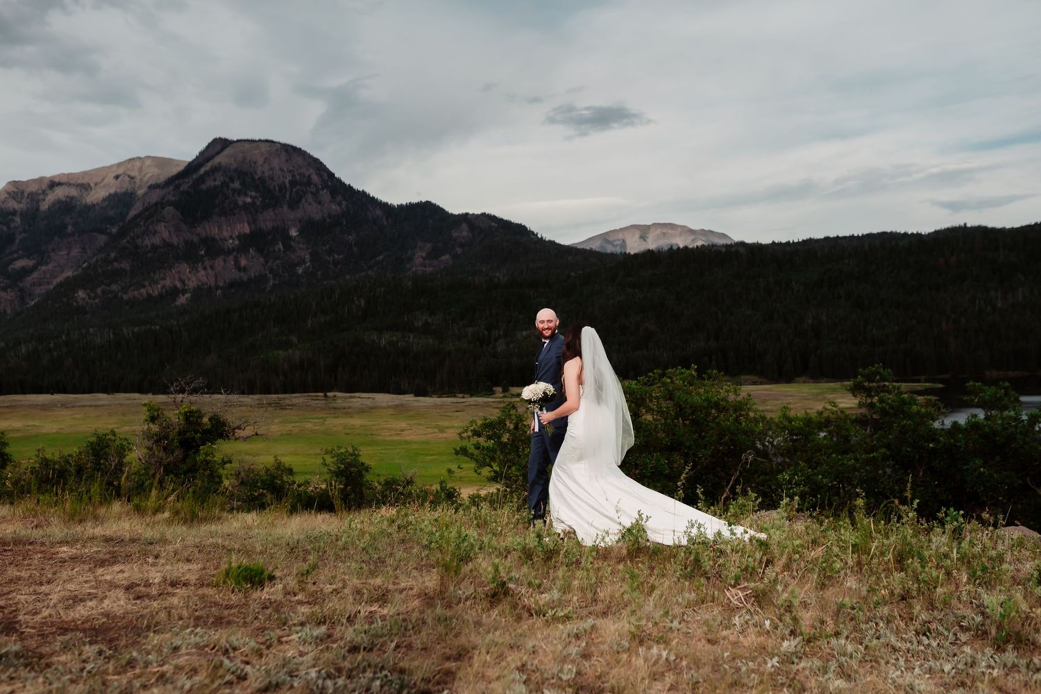 A couple walks hand in hand with mountain peaks creating a stunning backdrop for their wedding day.