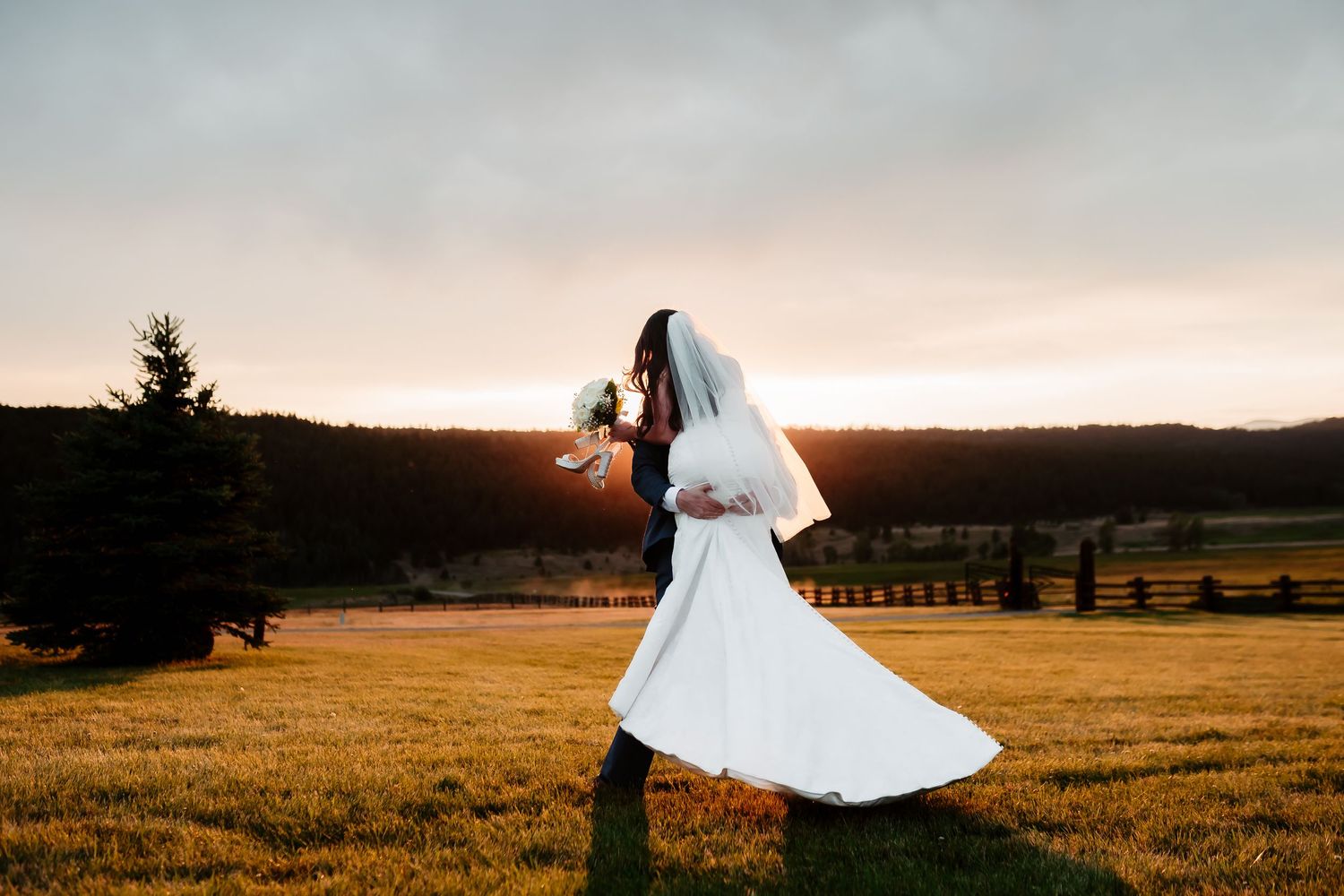 A bride twirls in her white dress against a golden sunset in a mountain meadow.