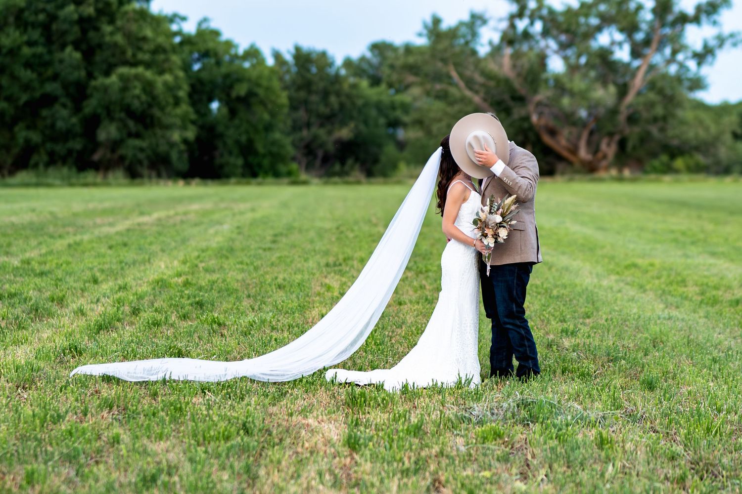 A couple sharing a tender moment on a grassy field with a flowing white wedding dress train.