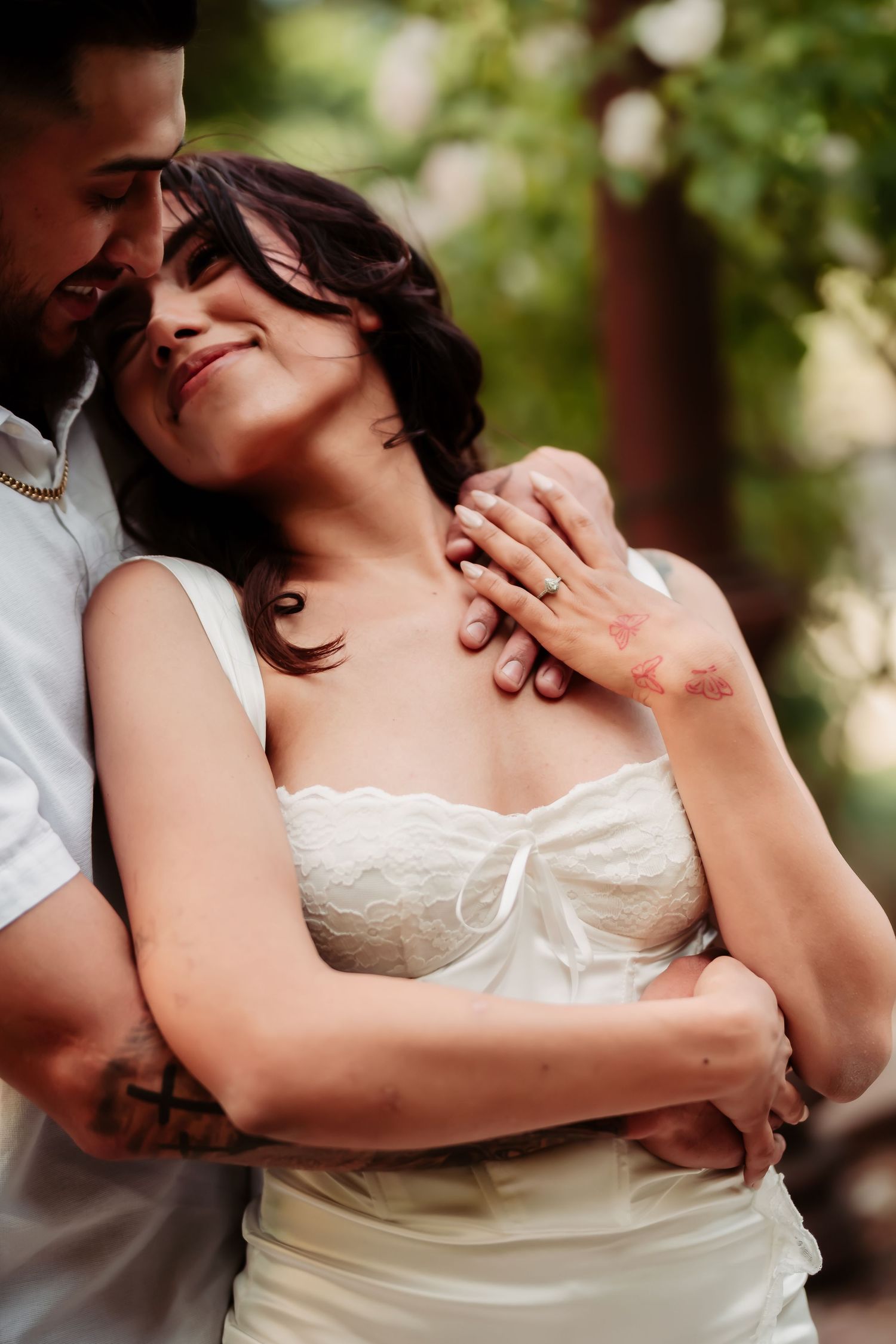 An affectionate couple shares a tender moment while embracing outdoors near garden foliage.