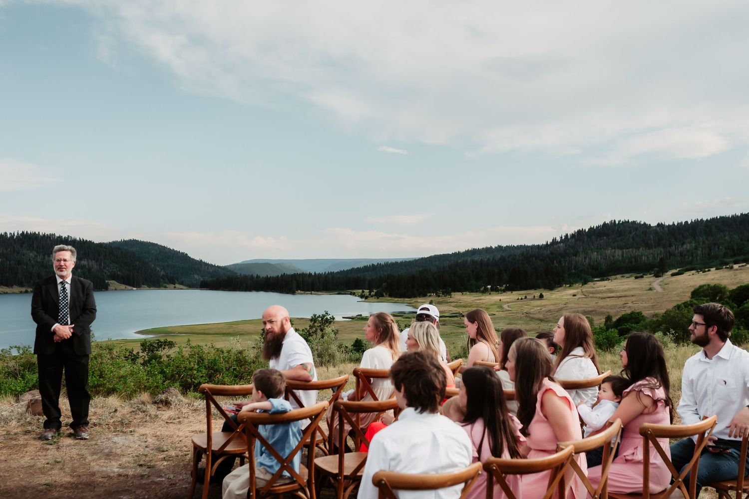 Outdoor wedding ceremony overlooking scenic mountain landscape with guests seated on white chairs.