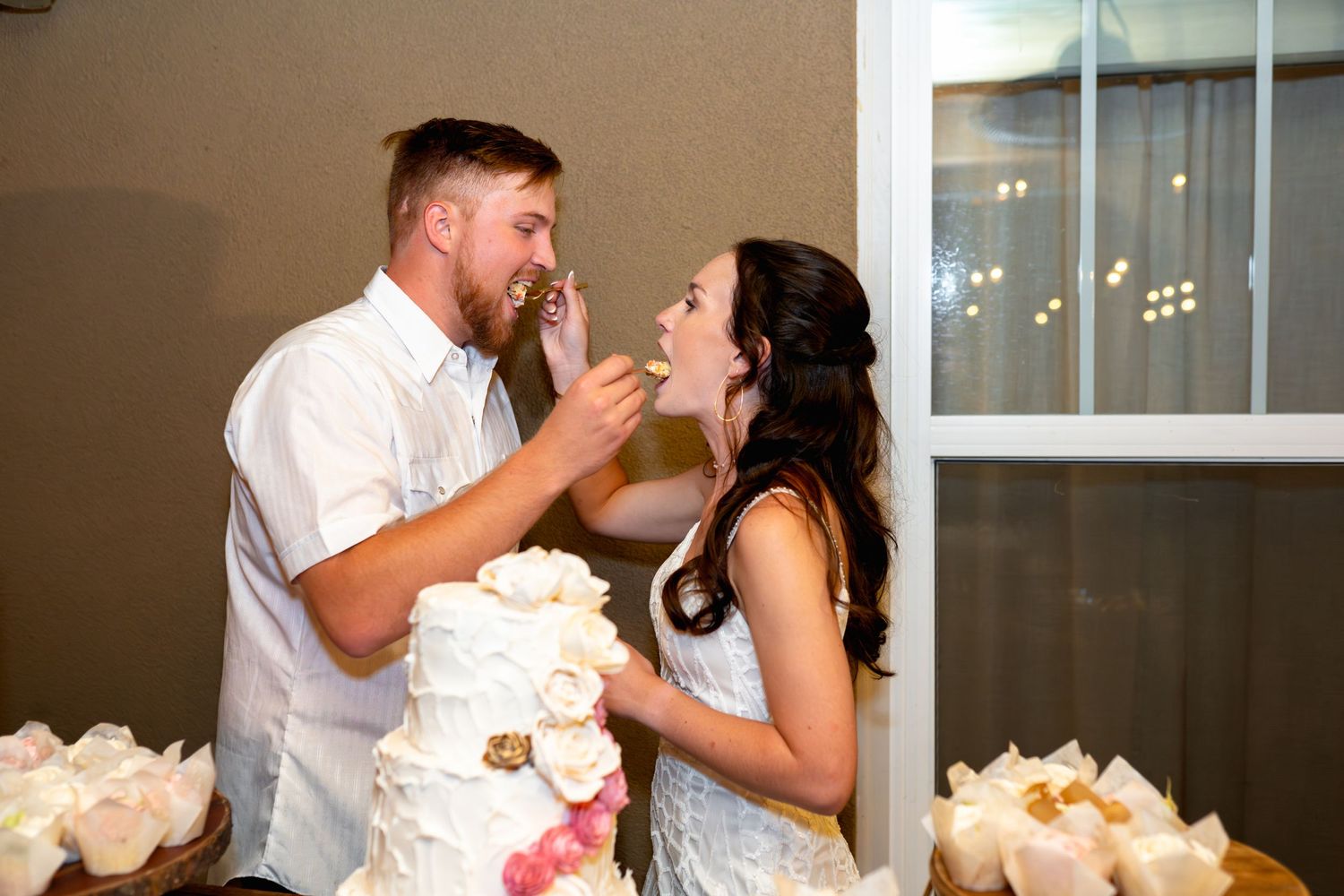 A newlywed couple playfully feeds each other wedding cake at their reception.