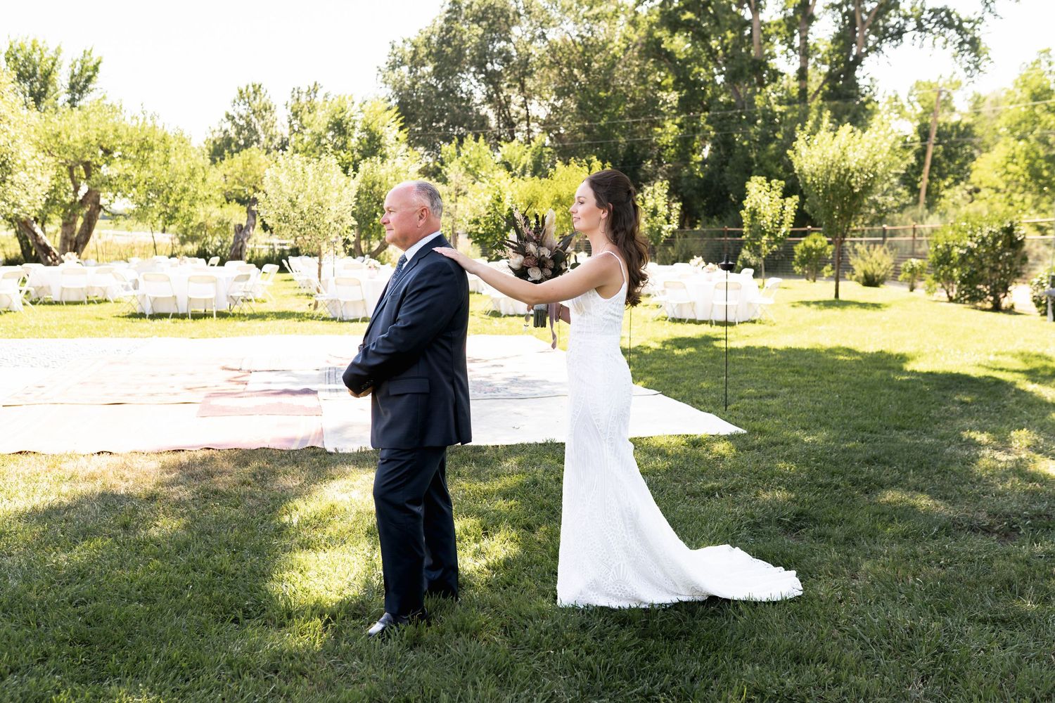 A wedding first look moment captured outdoors on a sunny day with green trees in the background.